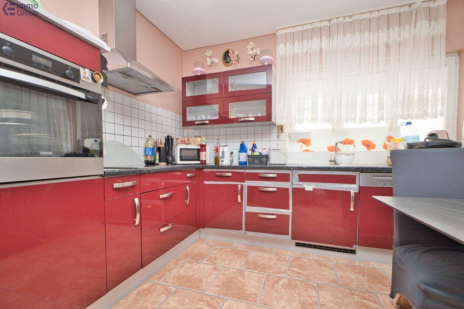 Rote Küche mit glänzenden Schränken, integriertem Backofen und weißem Fliesenspiegel.