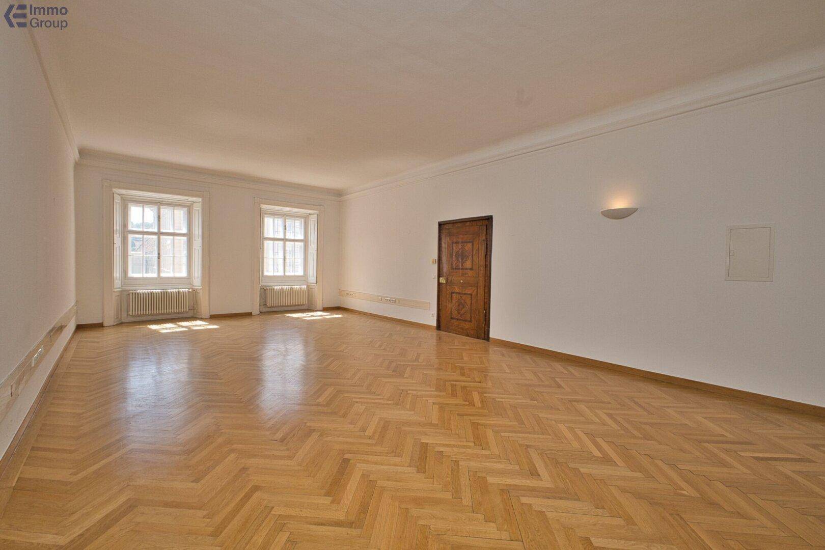 Heller, leerer Raum mit elegantem Fischgrätparkett und einer Holztür, die den klassischen Stil unterstreicht.