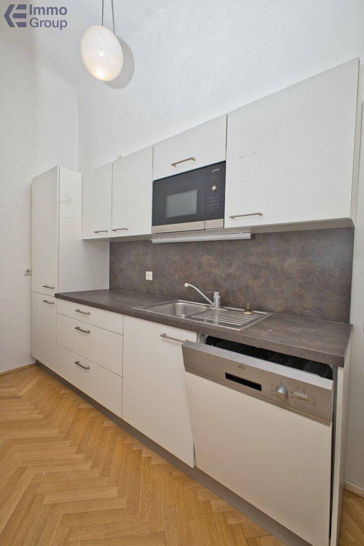 Moderne Küche mit weißen Schränken, dunkler Arbeitsplatte und integrierten Geräten auf Fischgrätparkett.
