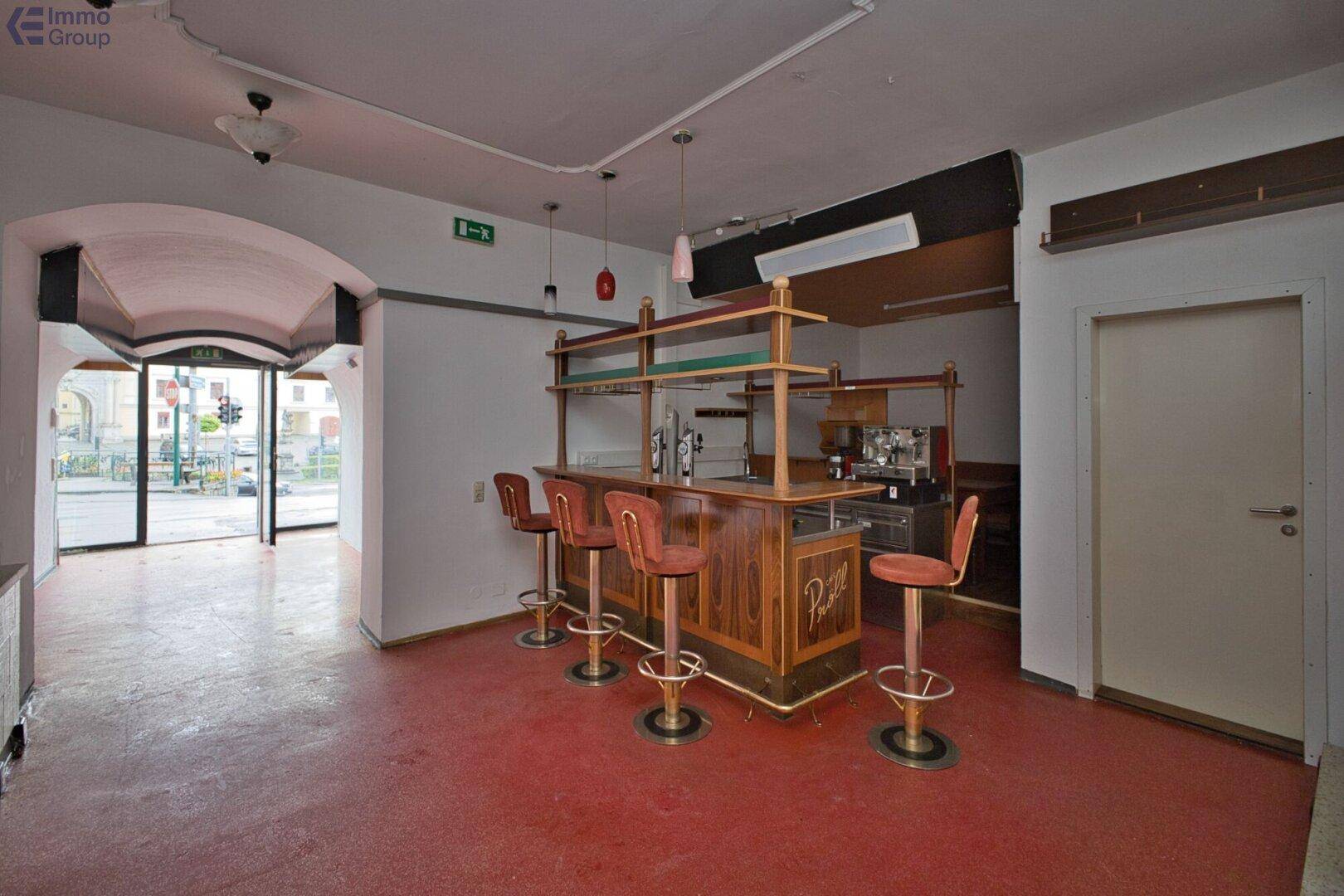 Innenansicht einer Bar oder eines Cafés mit Theke, Barhockern und Blick zur Straße.