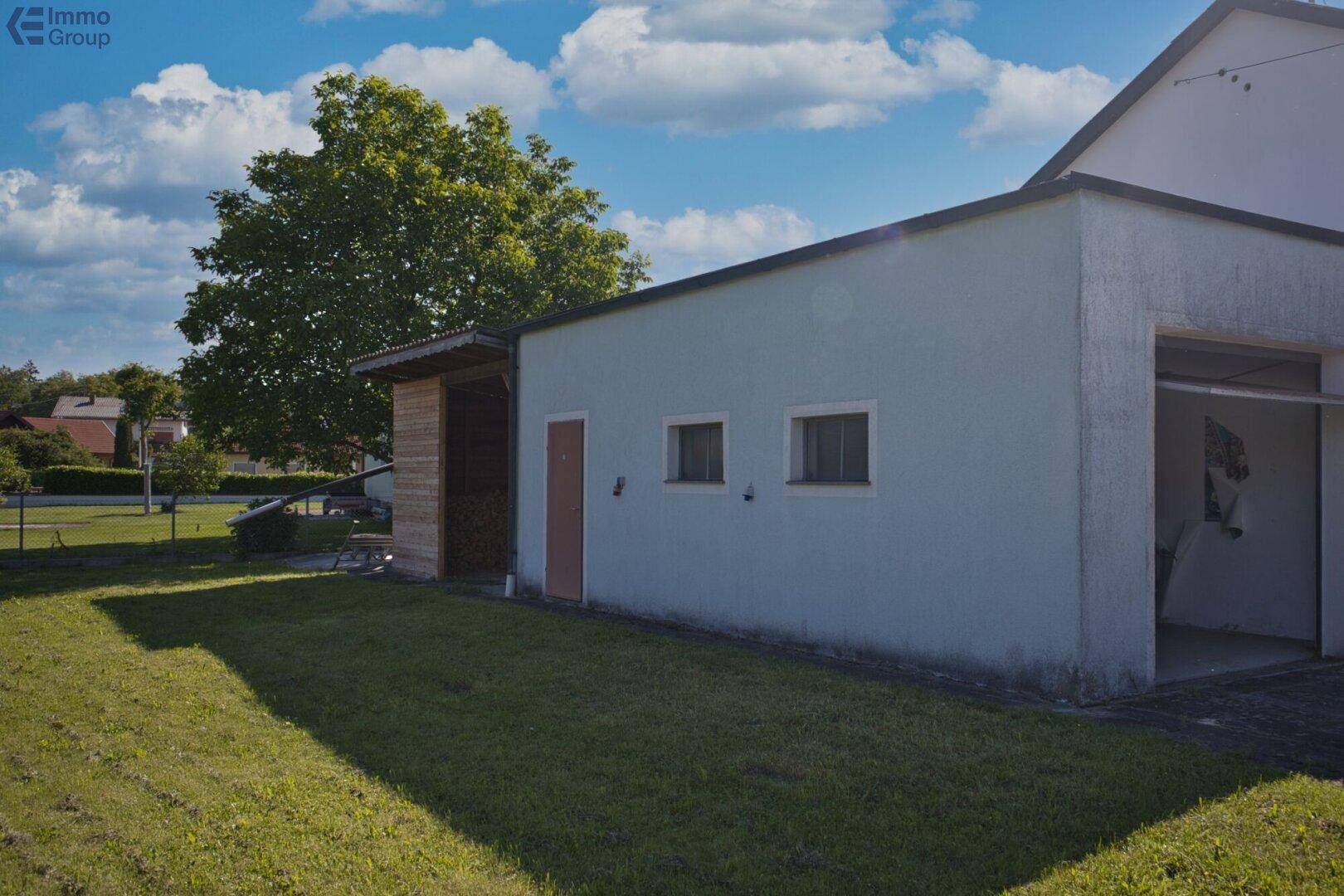 Nahaufnahme eines Nebengebäudes mit hellblauer Fassade und angrenzendem Holzschuppen auf einer Rasenfläche.