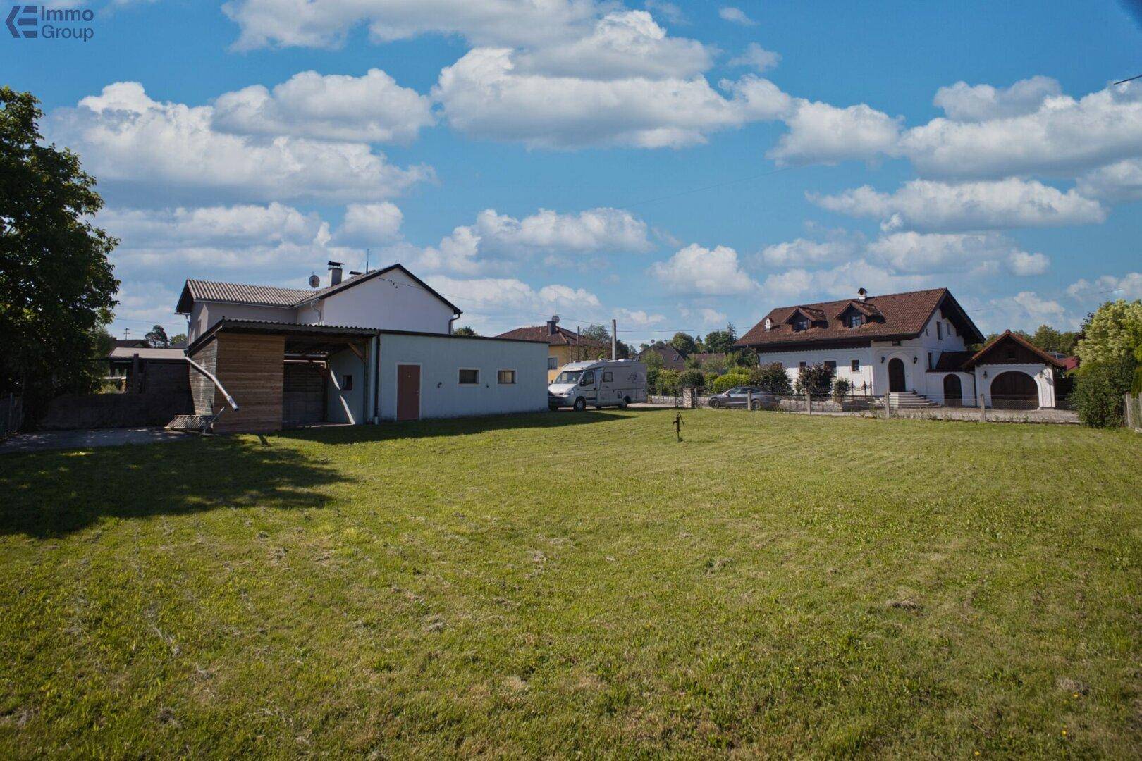 Weitläufige Rasenfläche mit Nebengebäude und Blick auf weitere Wohnhäuser in der Umgebung.