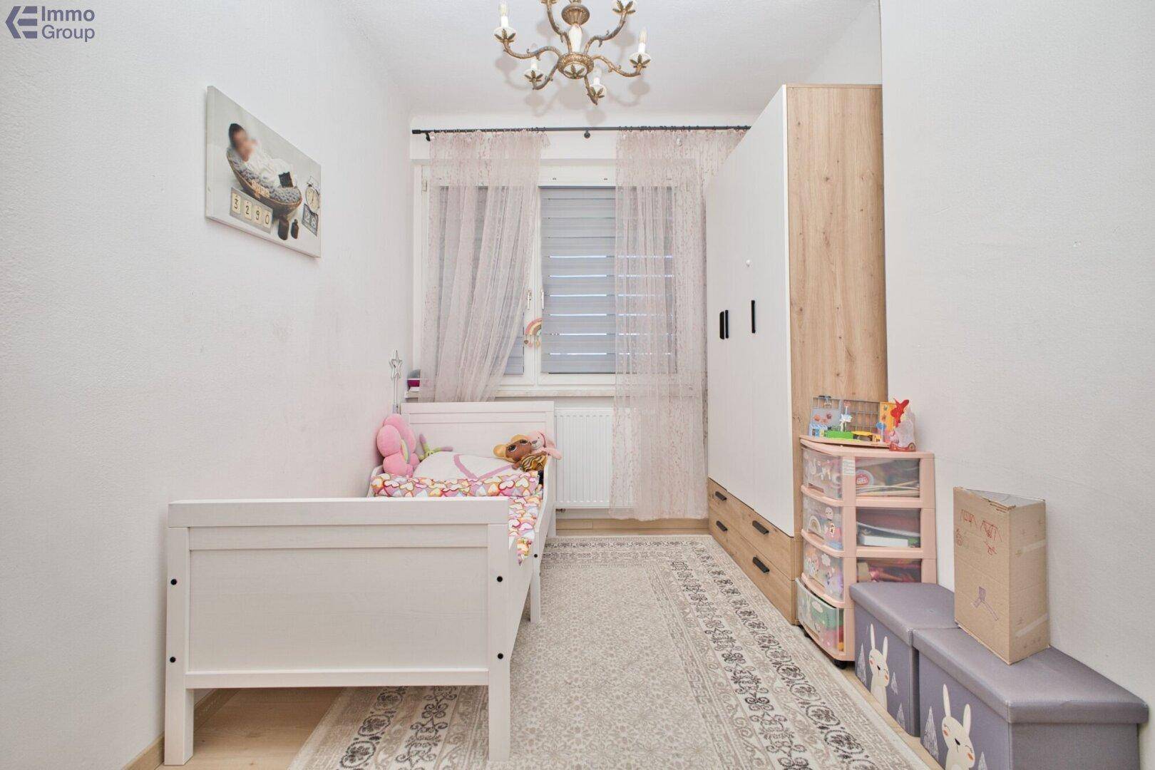 Helles Kinderzimmer mit weißem Bett, Kleiderschrank und Fenster mit Vorhängen.