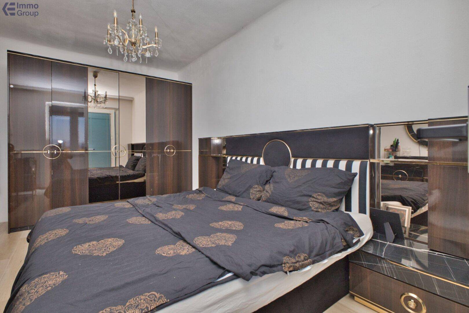 Schlafzimmer mit großem Bett, elegantem Kleiderschrank mit Spiegeltüren und Kronleuchter.