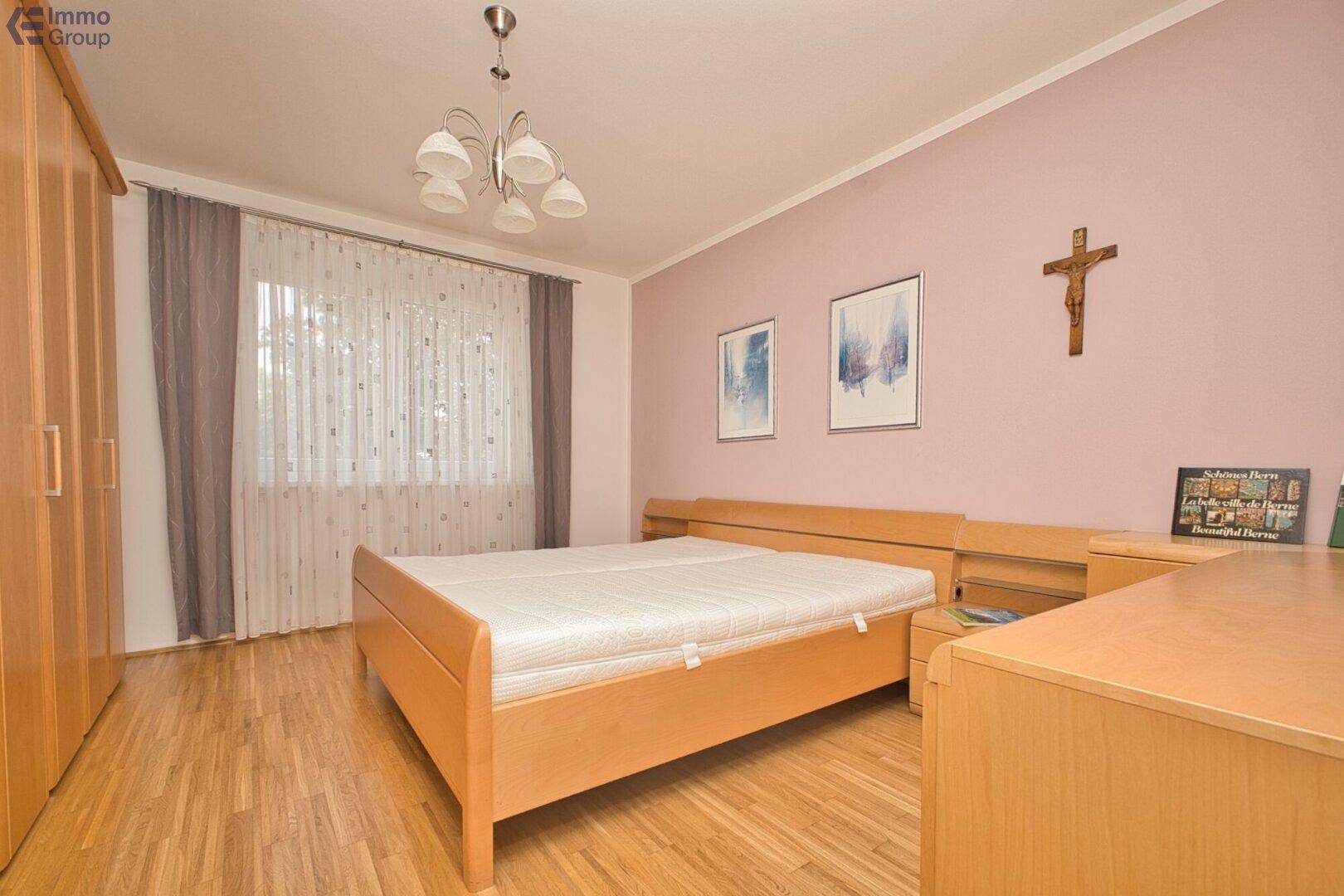 Schlafzimmer mit Holzbett, passenden Möbeln und rosa Wandakzenten.