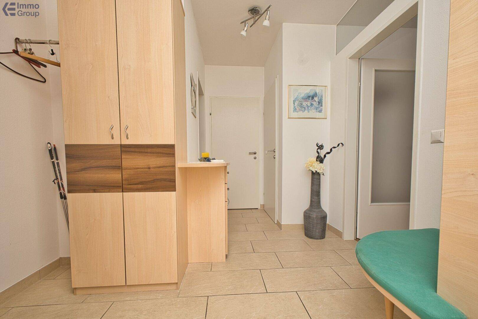 Eingangsbereich mit Fliesenboden, Holzschrank und dekorativer Vase.
