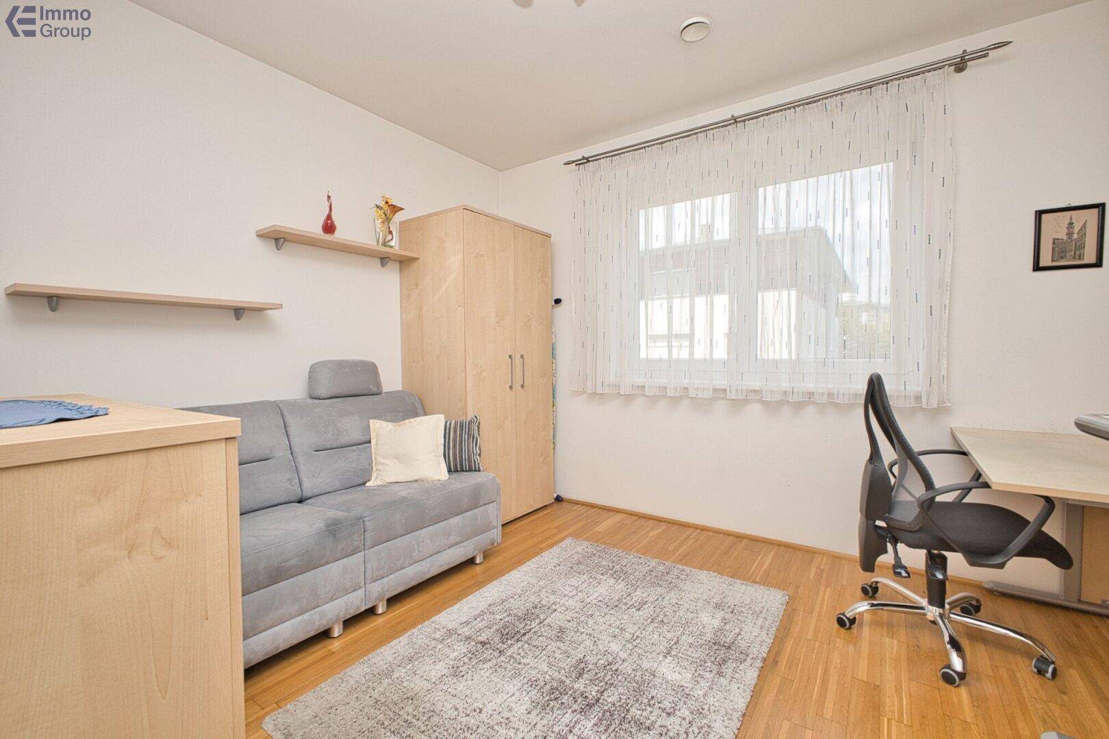 Helles Arbeitszimmer mit Holzboden, Schreibtisch und einem Schlafsofa.