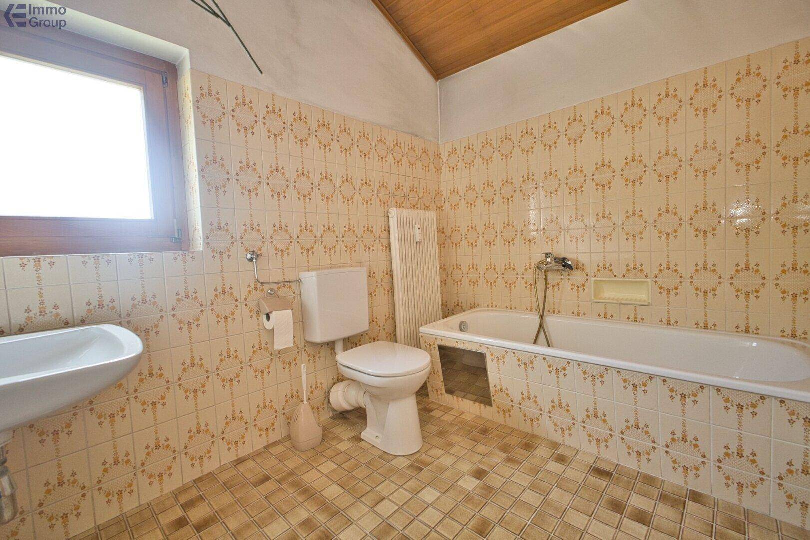 Badezimmer mit Badewanne, WC und Waschbecken, gefliest im Stil der 80er Jahre.