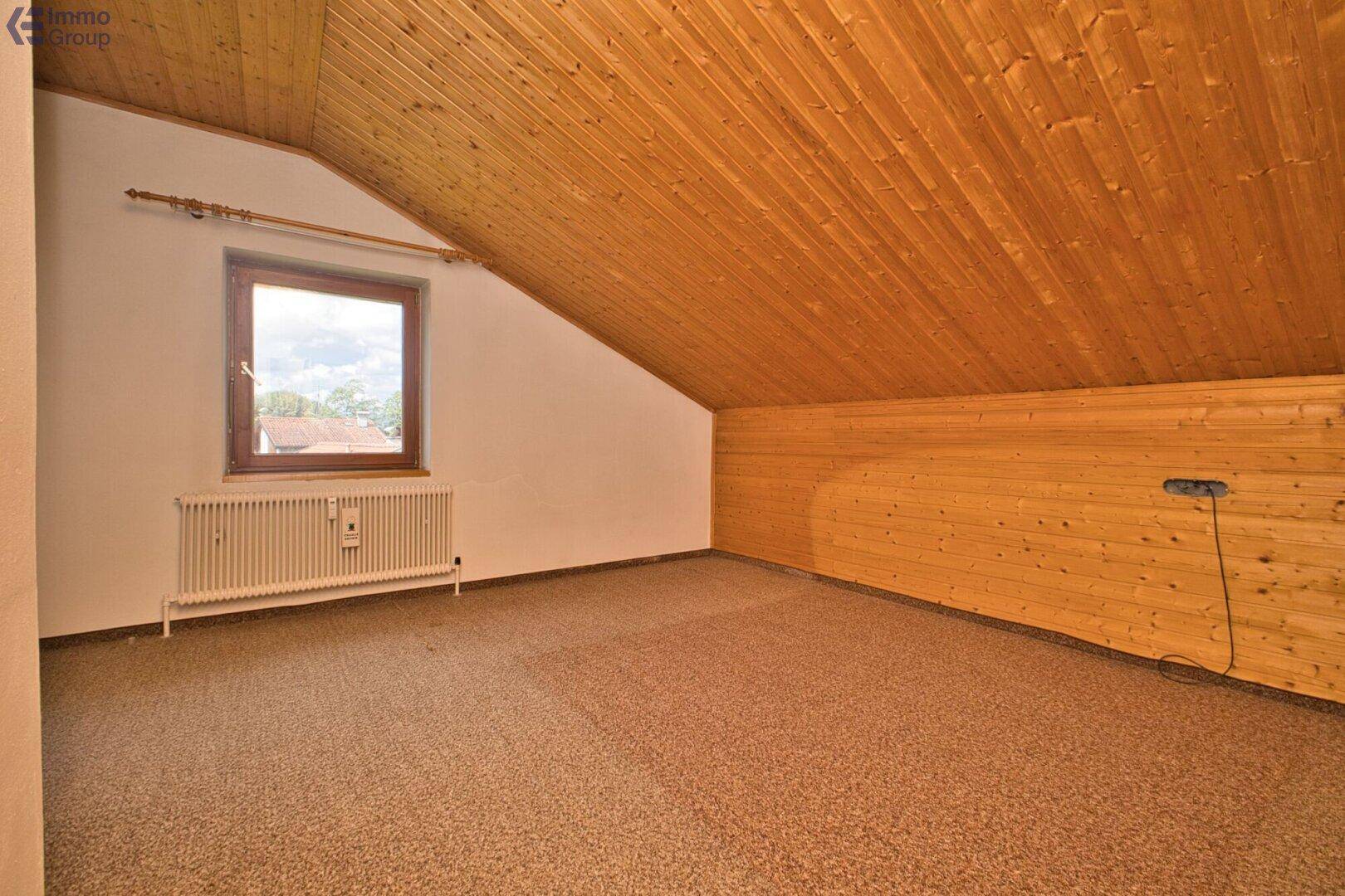 Dachgeschosszimmer mit Holzverkleidung, Teppichboden und schrägen Wänden.