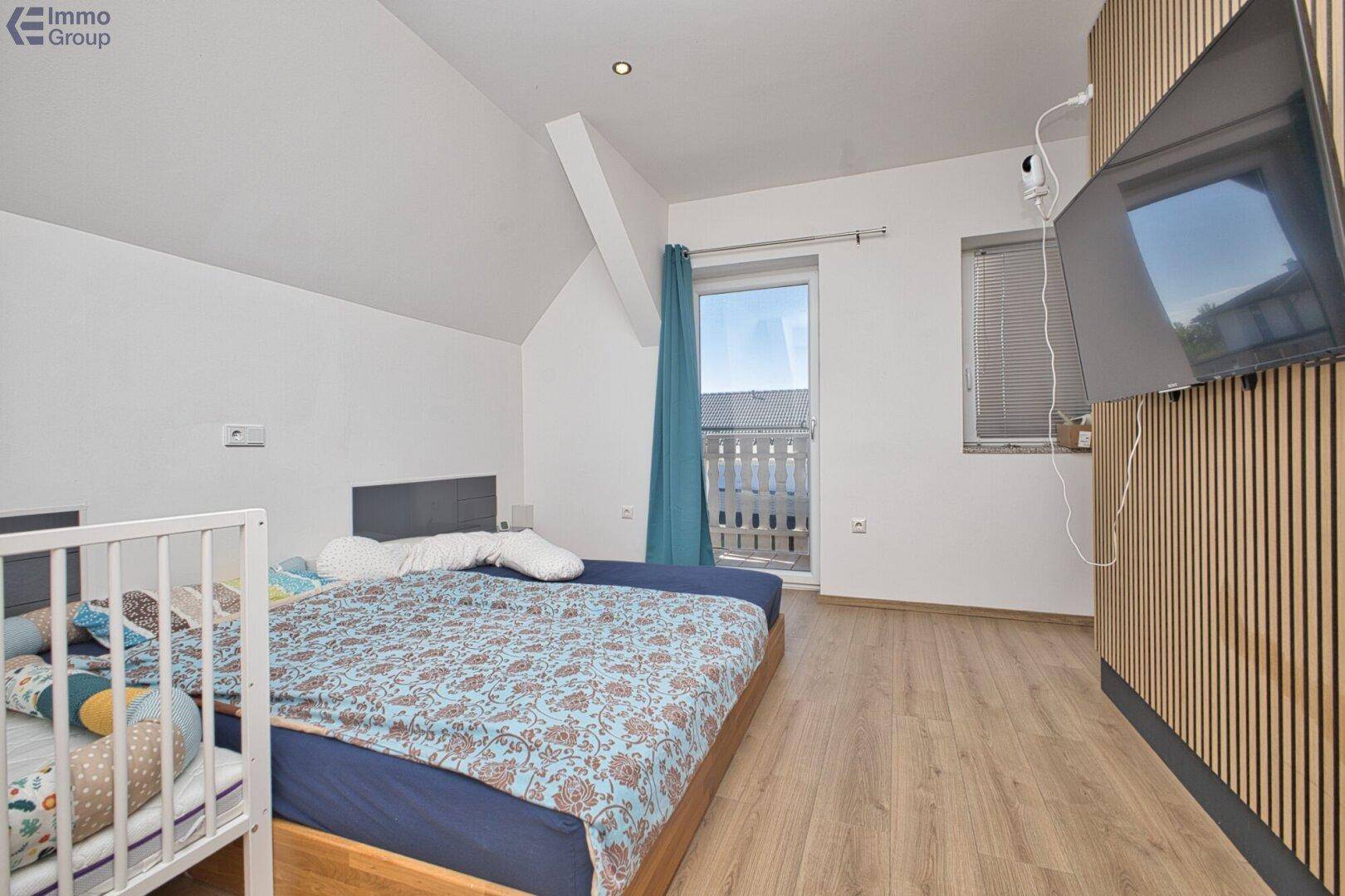 Helles Schlafzimmer mit Holzboden, Dachschräge und Zugang zu einem kleinen Balkon.