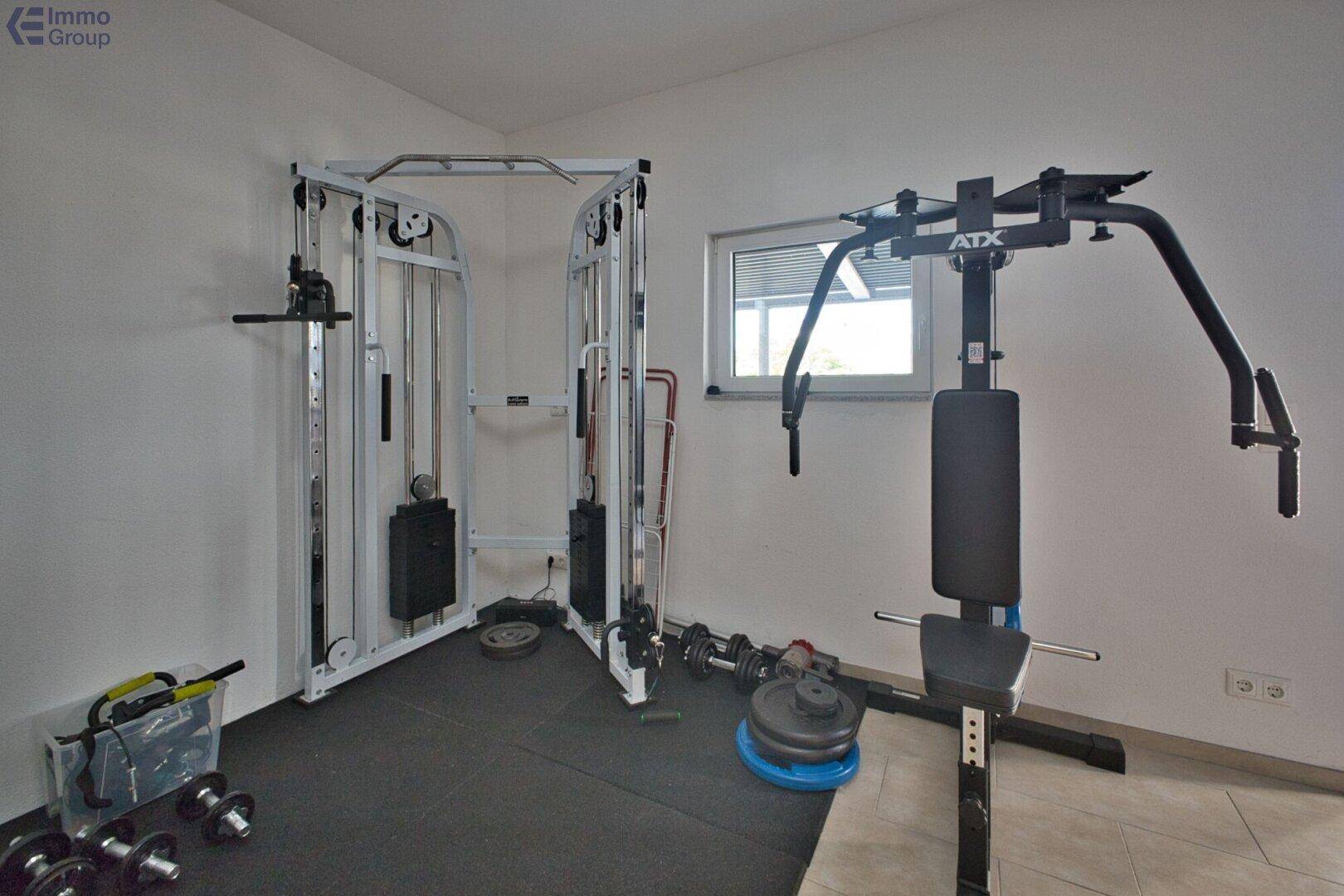 Privater Fitnessraum mit verschiedenen Trainingsgeräten und Fenster für Tageslicht.