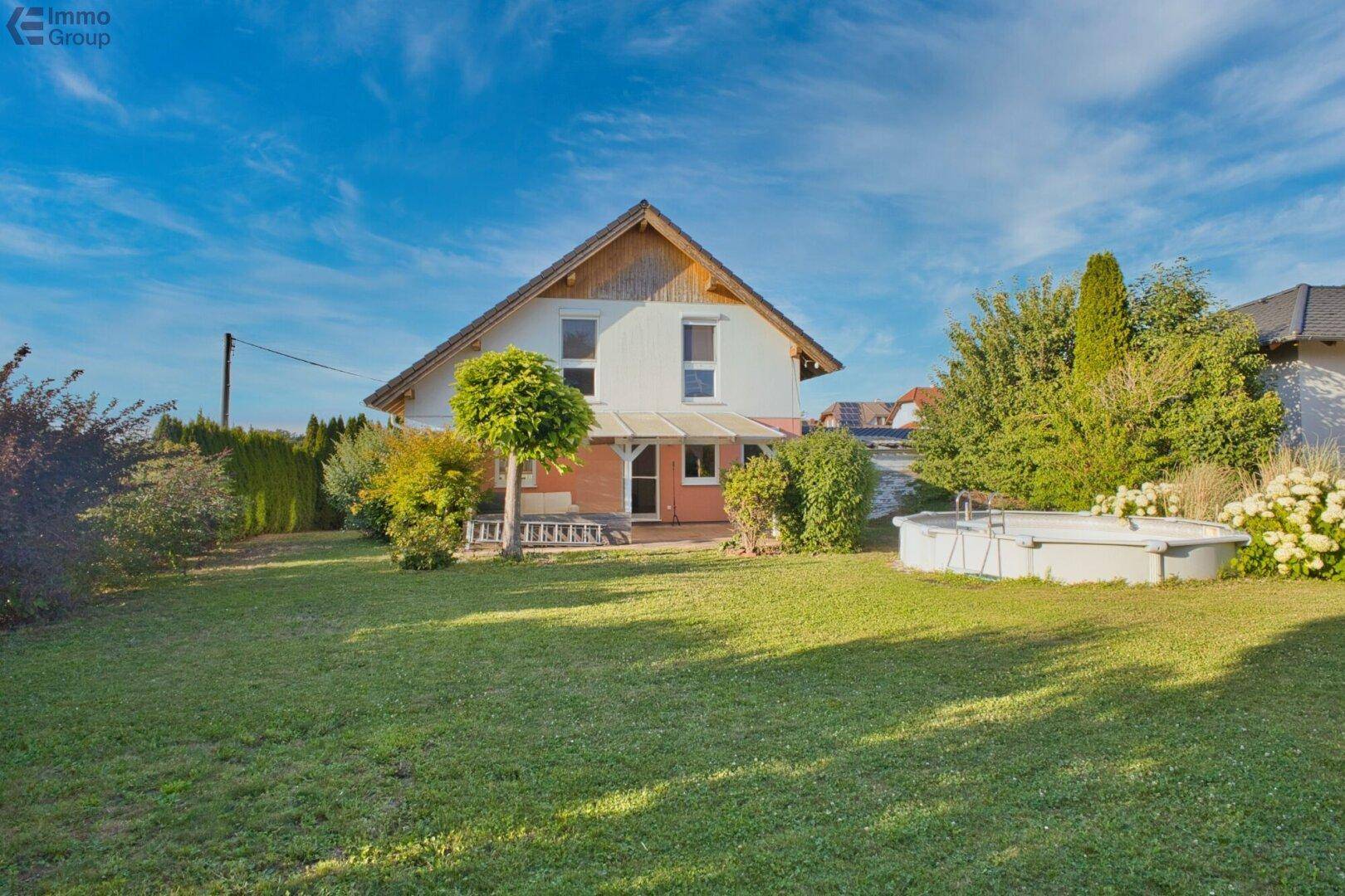 Rückansicht des Hauses mit großem Rasenbereich, kleinem Pool und blühenden Sträuchern im Garten.