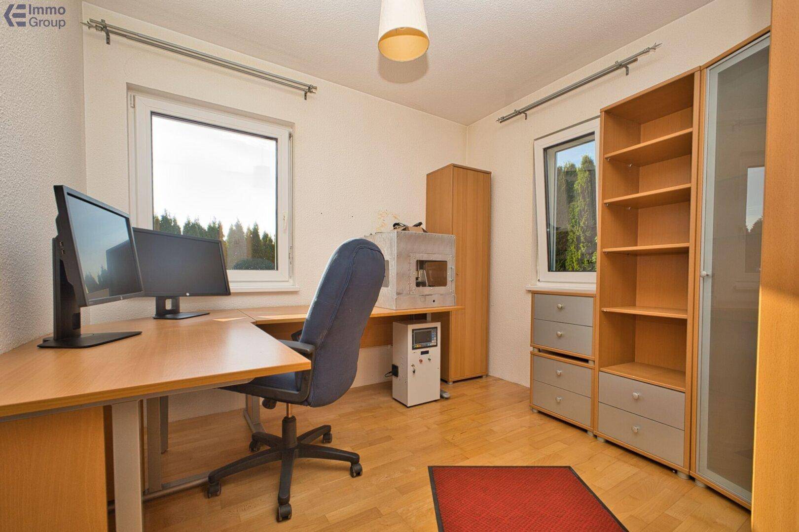 Funktionales Arbeitszimmer mit Holzboden, zwei Fenstern und Regalsystem für Stauraum.