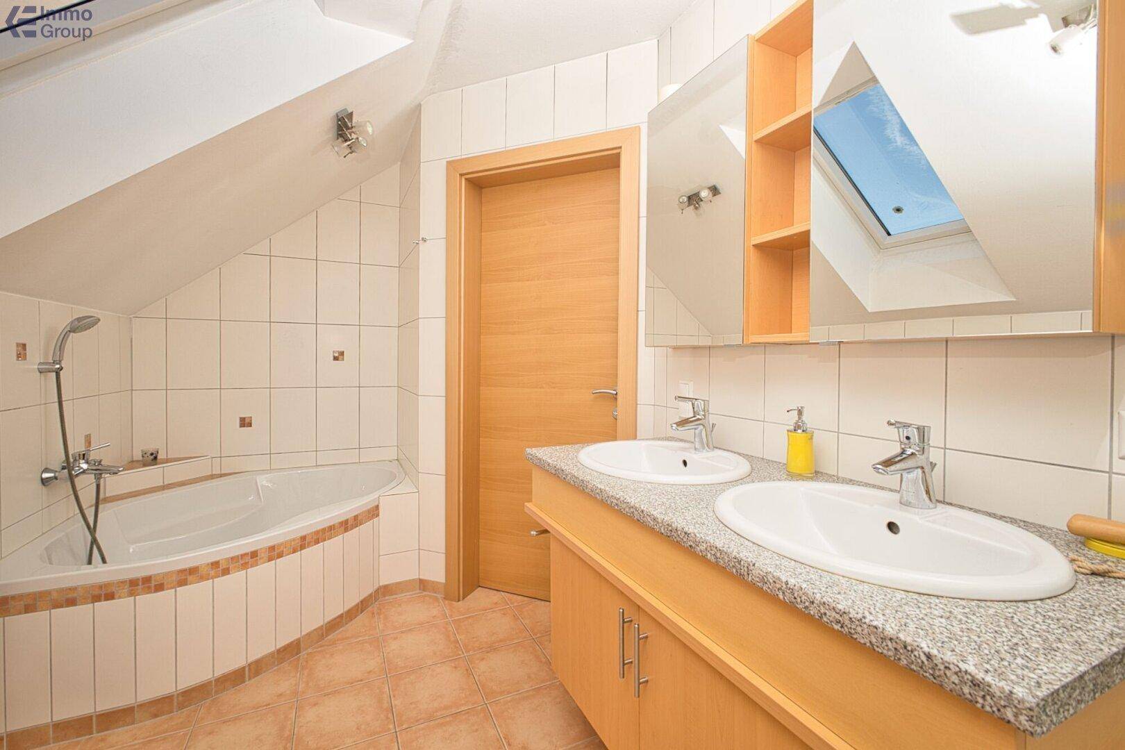 Badezimmer im Dachgeschoss mit Doppelwaschbecken, Badewanne und Dachfenster für Tageslicht.