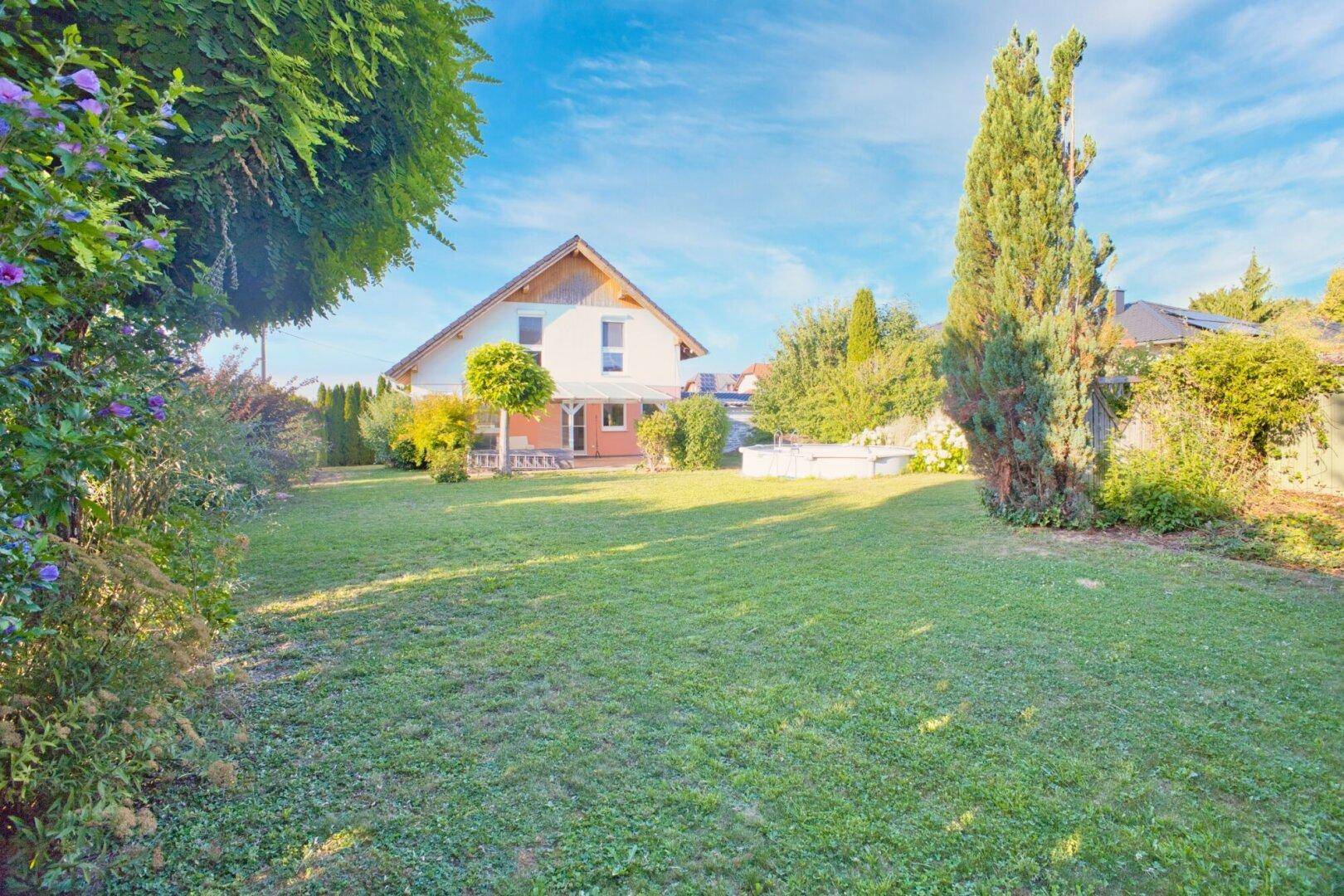 Weitläufiger Gartenbereich mit Rasenfläche, hohen Bäumen und Blick auf das Einfamilienhaus.