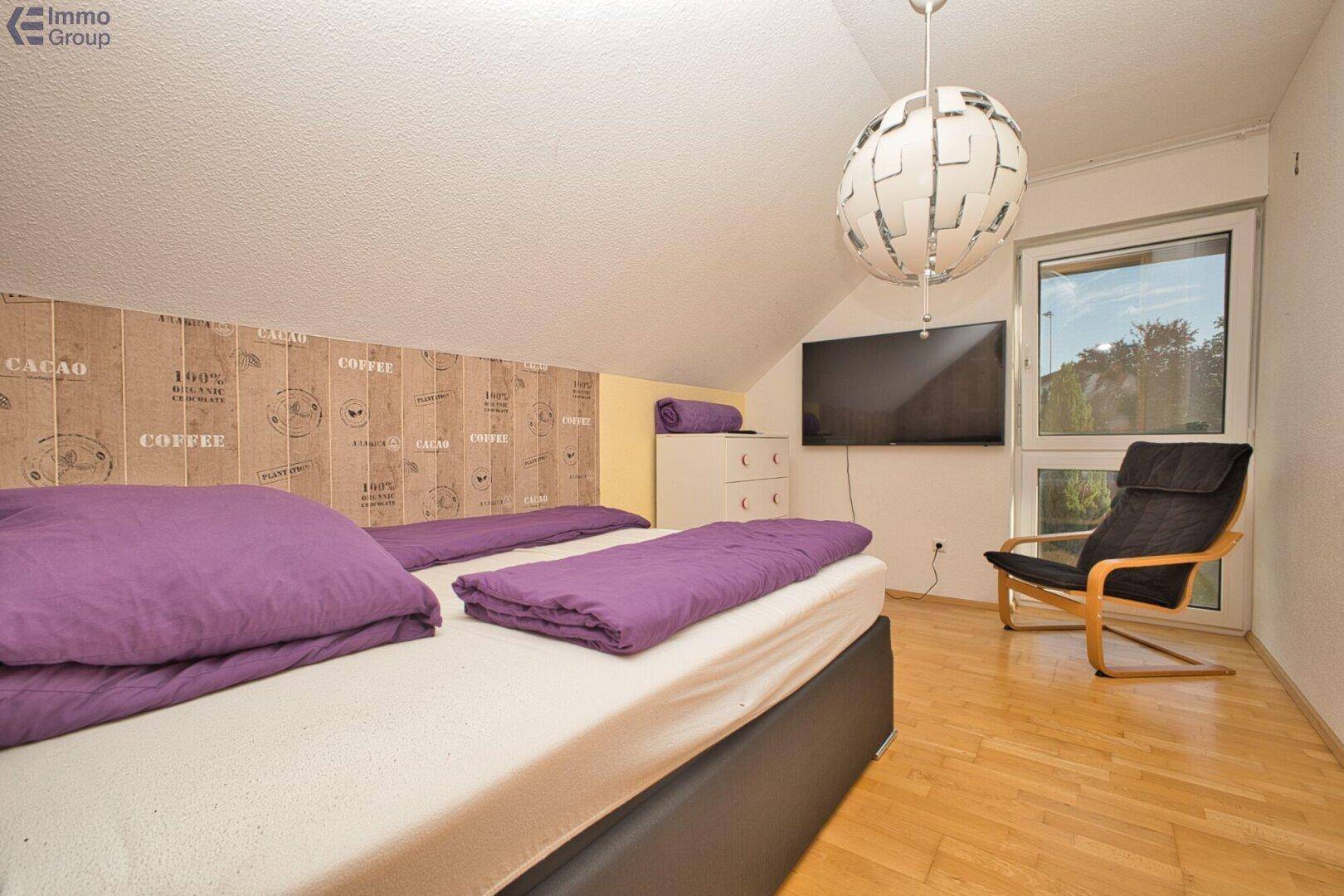 Helles Schlafzimmer mit Holzboden, lila Bettwäsche und modernem Deckenlicht im Dachgeschoss.