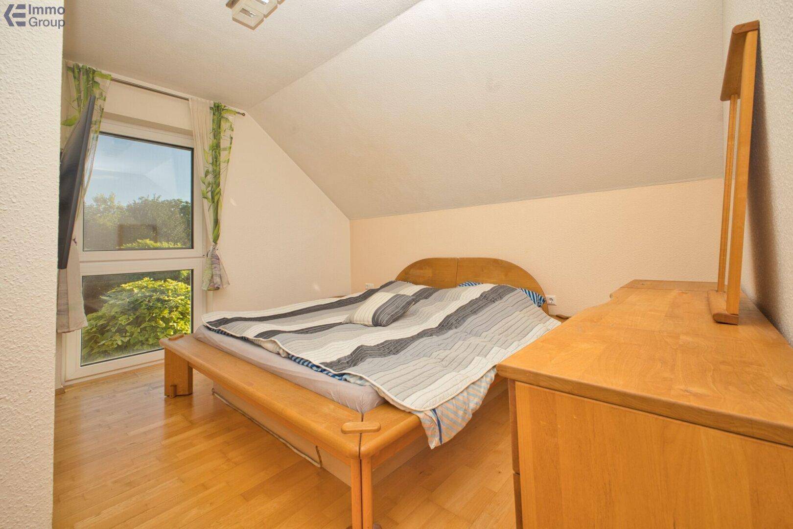 Schlafzimmer im Dachgeschoss mit Holzboden, großem Fenster und schräger Decke.