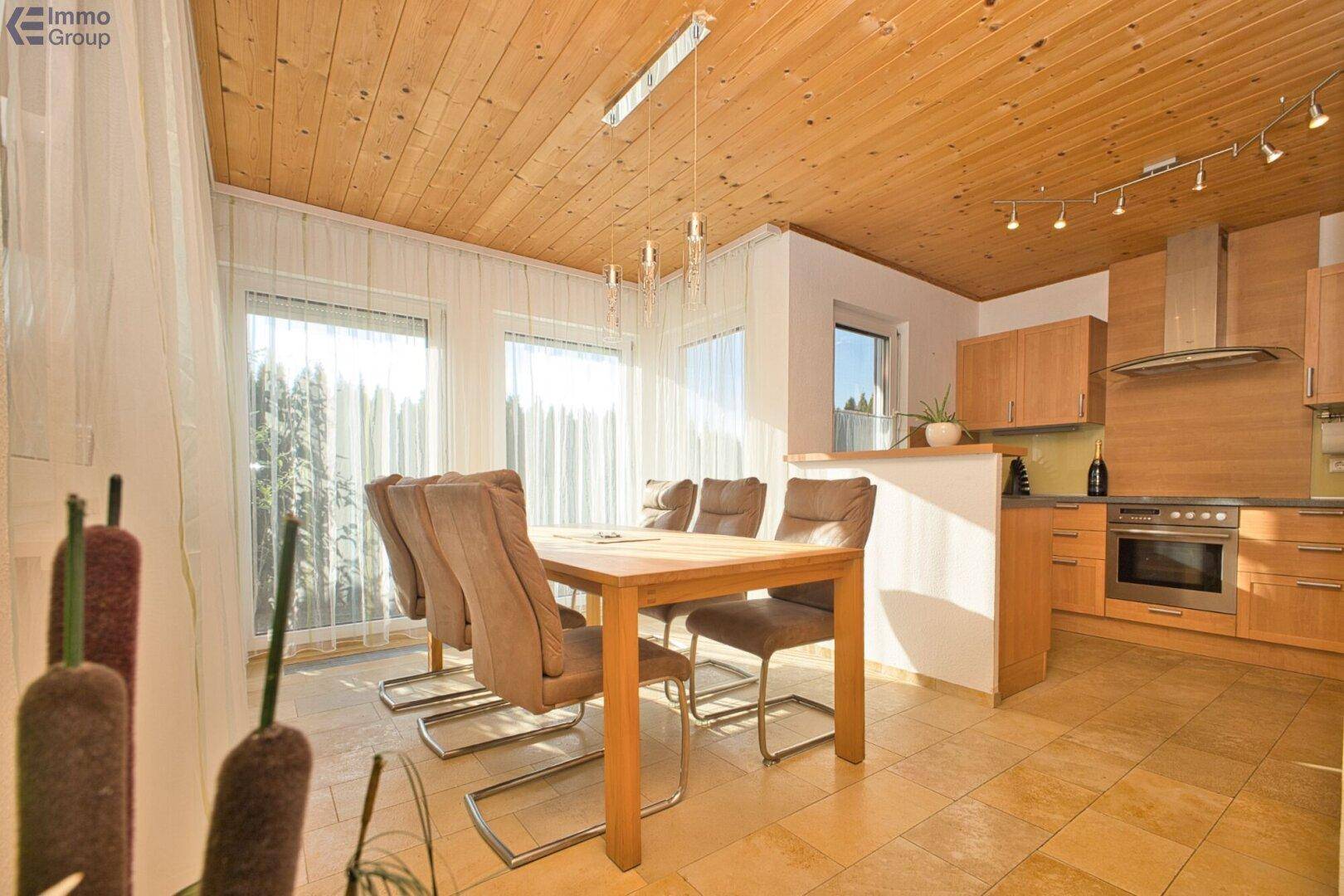 Heller Essbereich mit Holztisch, Stühlen und offener Küche mit Holzdeckenverkleidung.