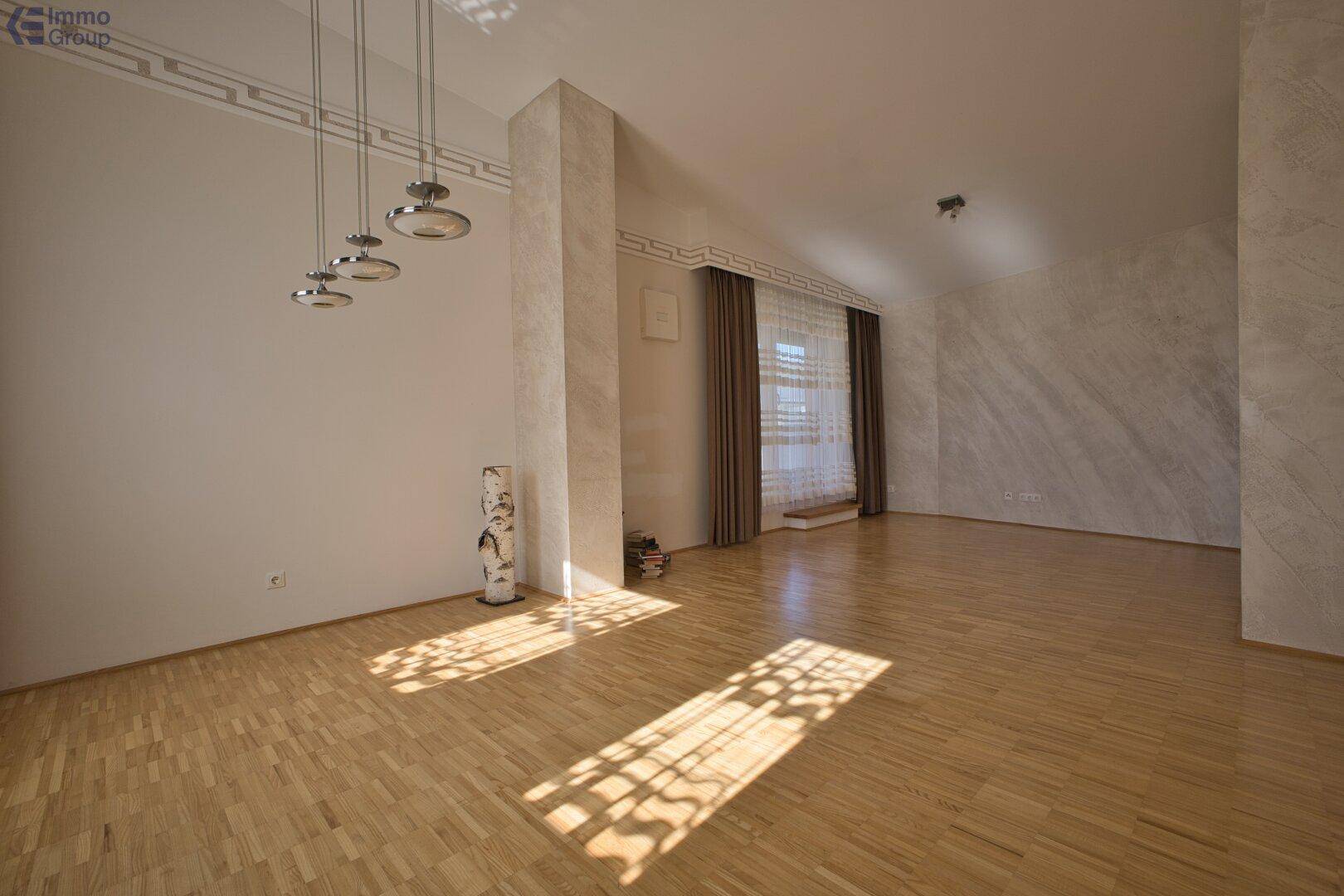 Heller, leerer Wohnraum mit Holzboden, großen Fenstern und viel natürlichem Lichteinfall.
