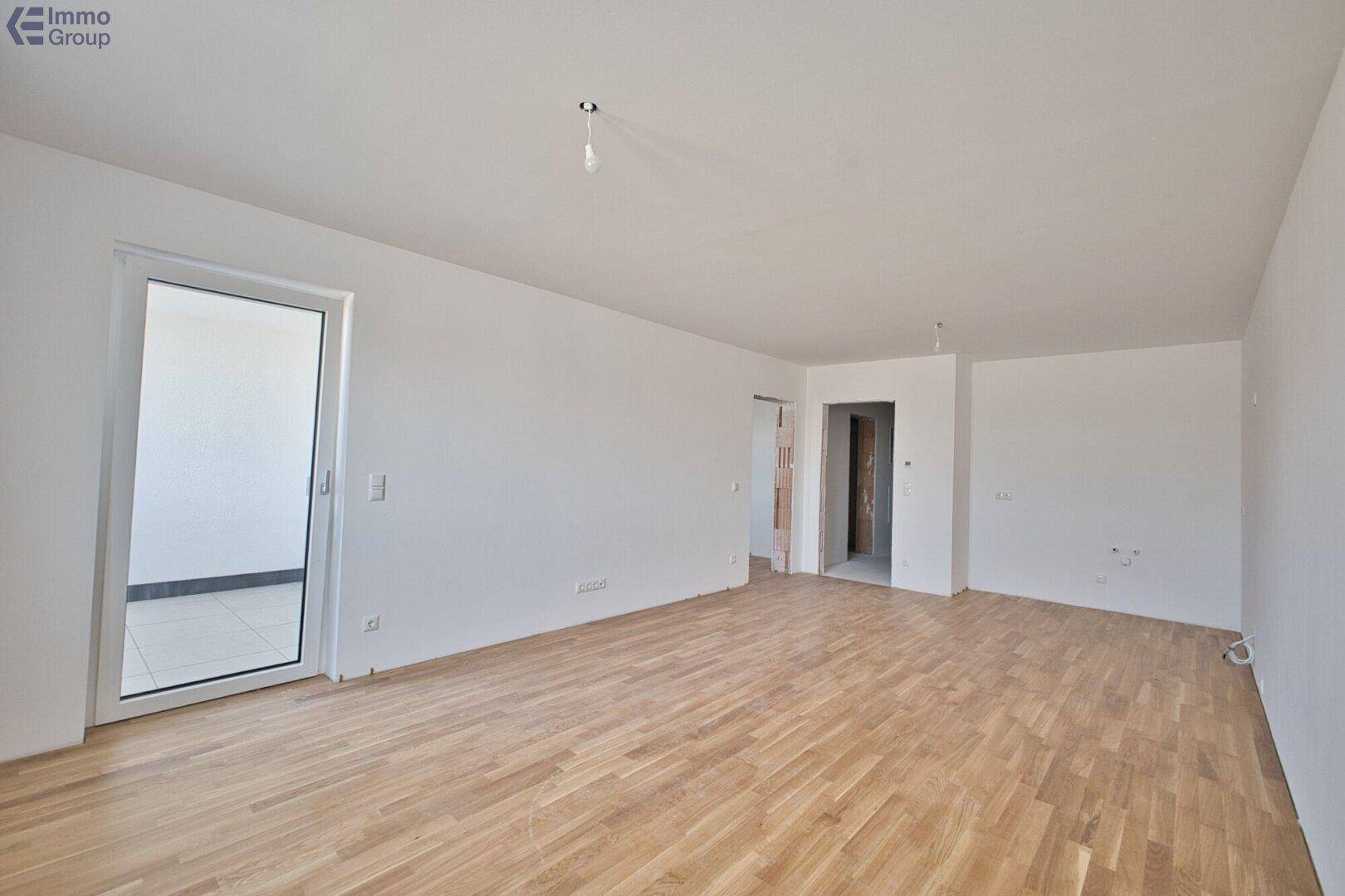 Geräumiges, leeres Wohnzimmer mit hellem Holzboden und Zugang zu einem Außenbereich.