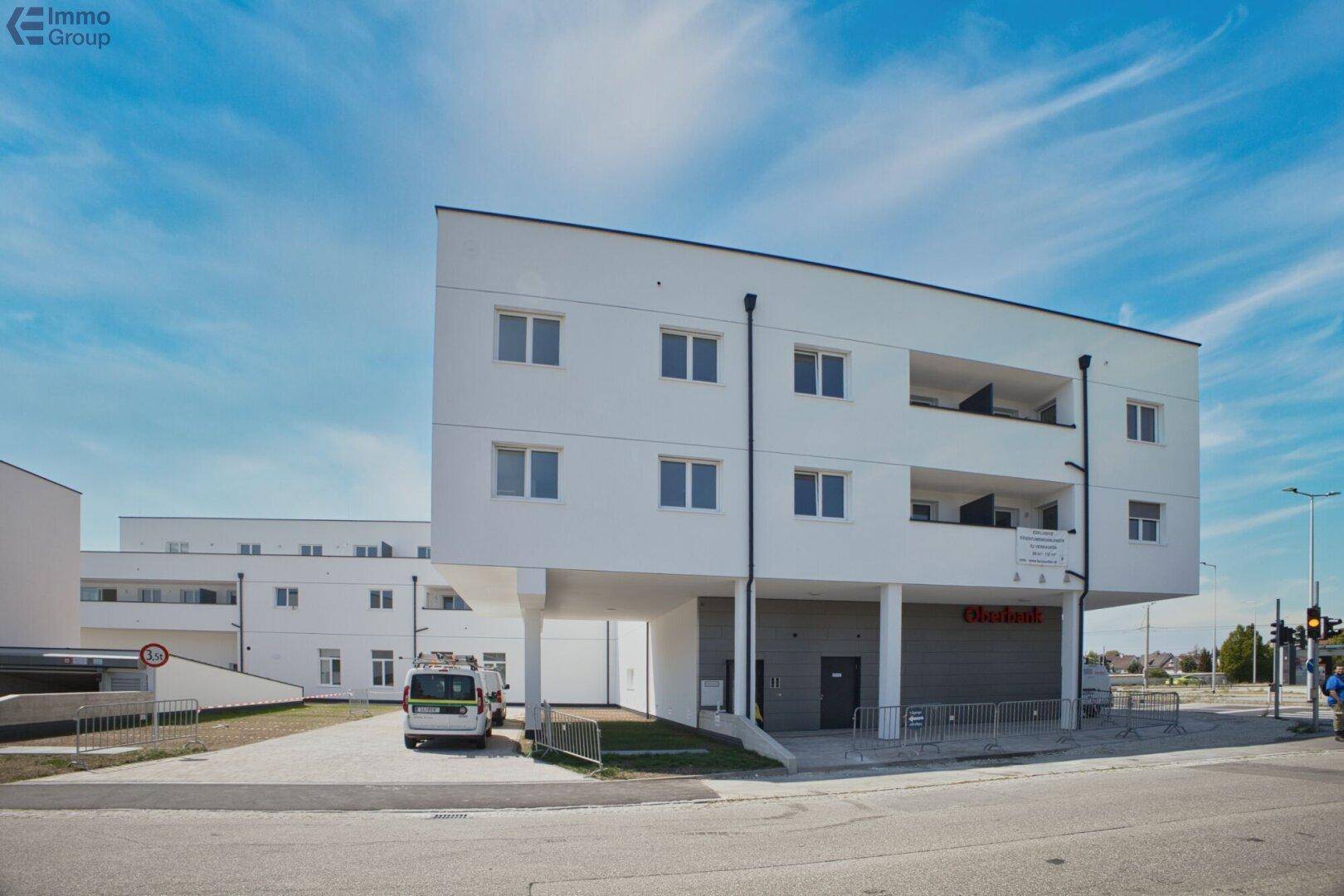 Neubau mit moderner Architektur, weißer Fassade und großzügigen Balkonen in städtischer Umgebung.