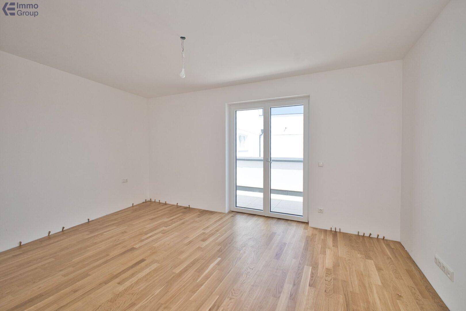 Lichtdurchfluteter Raum mit Holzparkett und großer Fenstertür, die Zugang zu einem Balkon bietet.