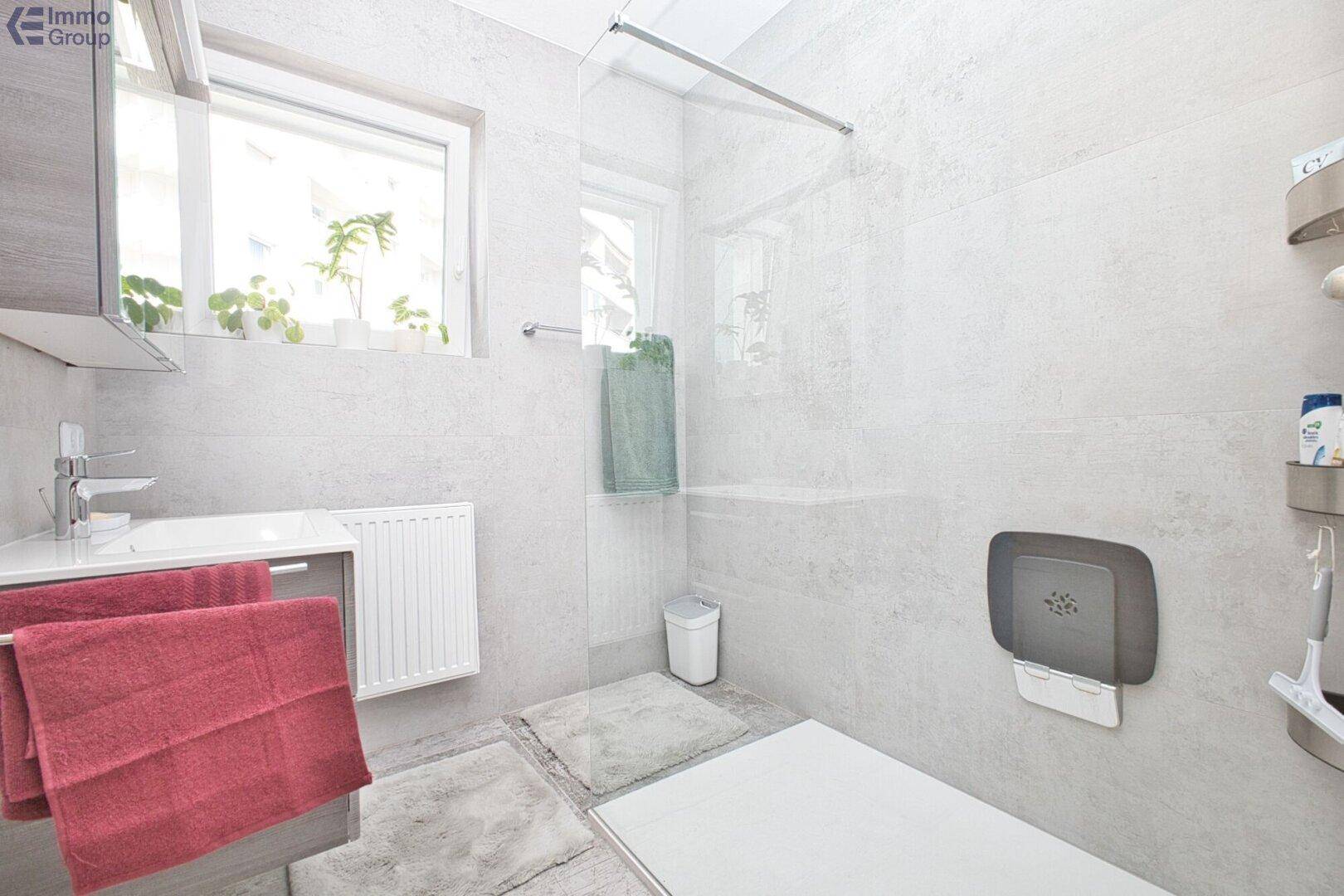 Modernes Badezimmer mit begehbarer Dusche, Fenster und hellen Fliesen an Wänden und Boden.