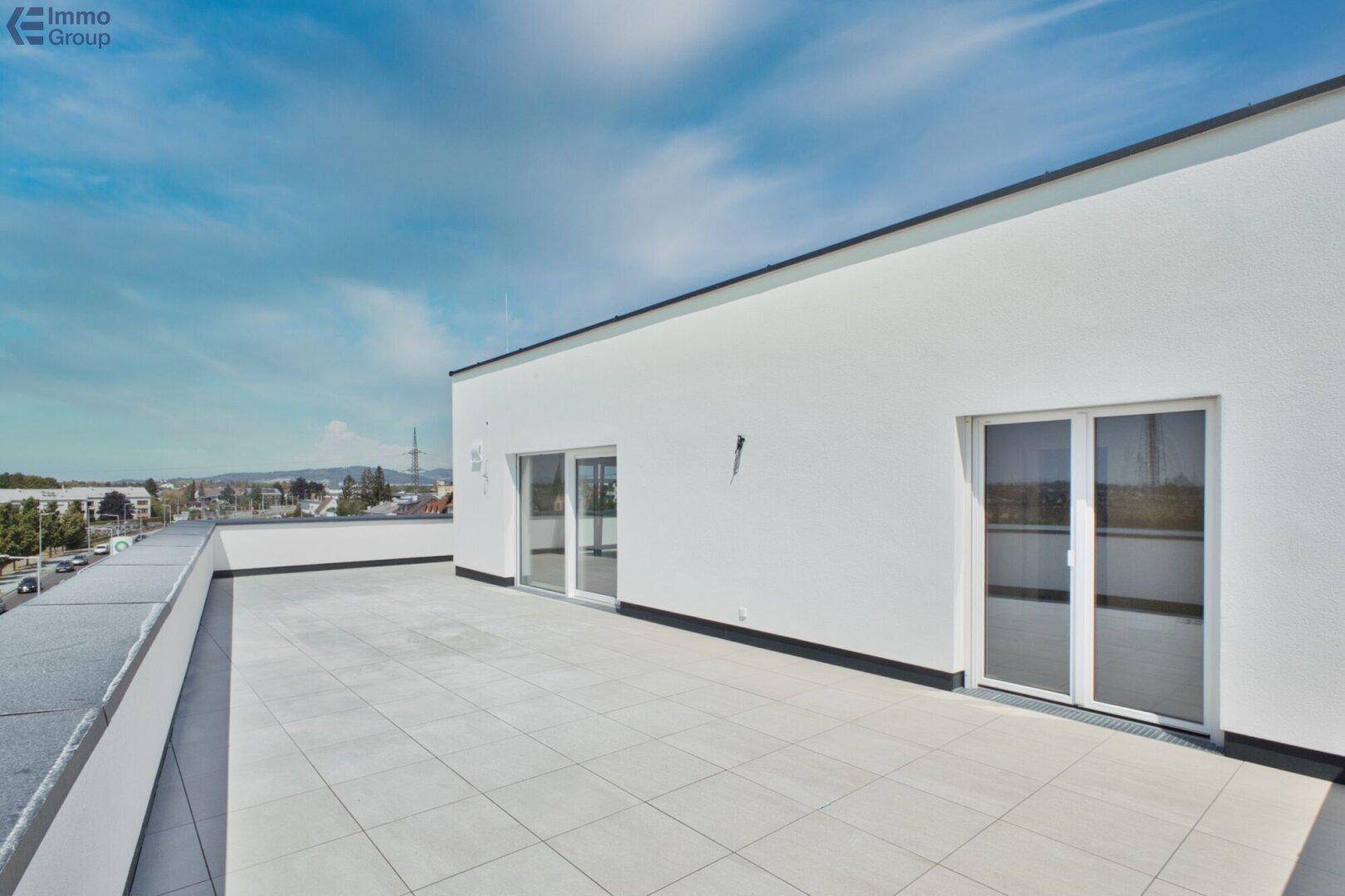 Geräumige Dachterrasse mit hellem Fliesenboden und großen Fenstertüren, die zum Innenbereich führen.