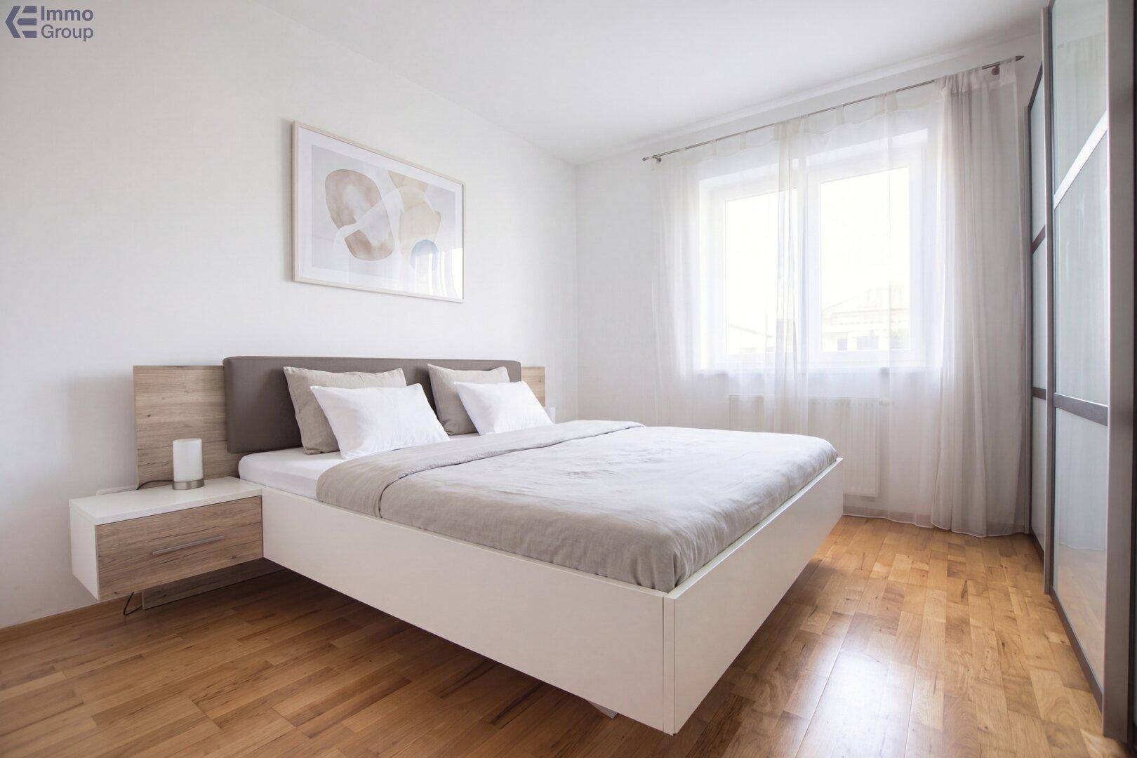 Helles Schlafzimmer mit Holzboden, großem Bett und Fenster mit Vorhängen.