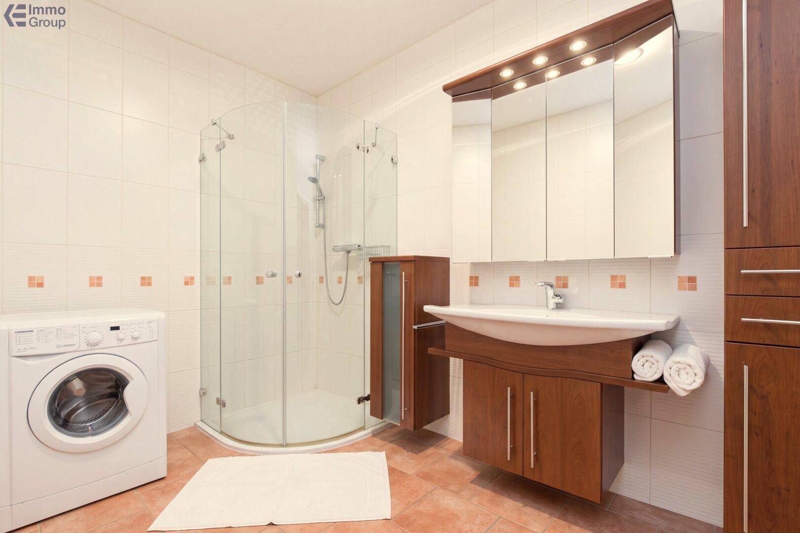 Badezimmer mit Duschkabine, Waschmaschine und Holzschränken.