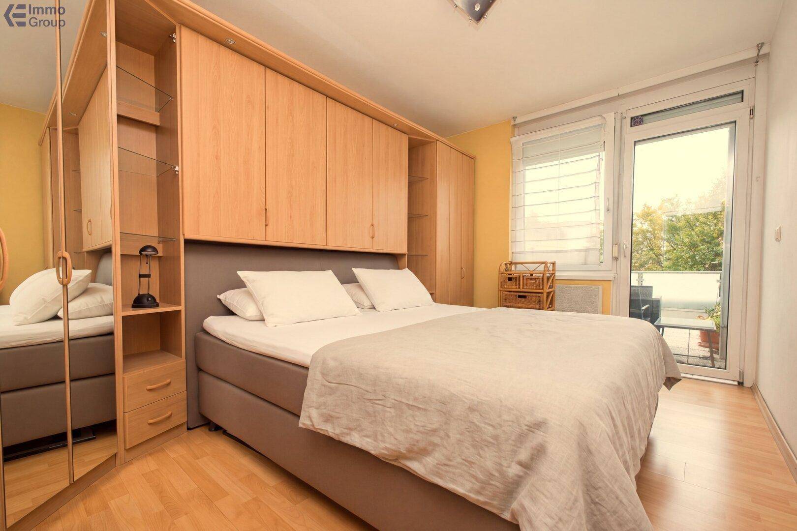 Schlafzimmer mit Einbauschränken, Holzboden und Zugang zu einem französischen Balkon.