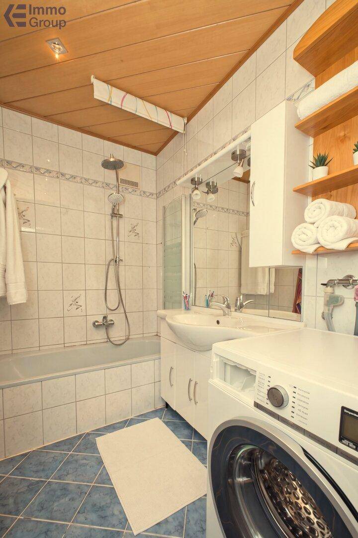 Badezimmer mit Badewanne, Dusche und Waschmaschine unter einer Holzdecke.
