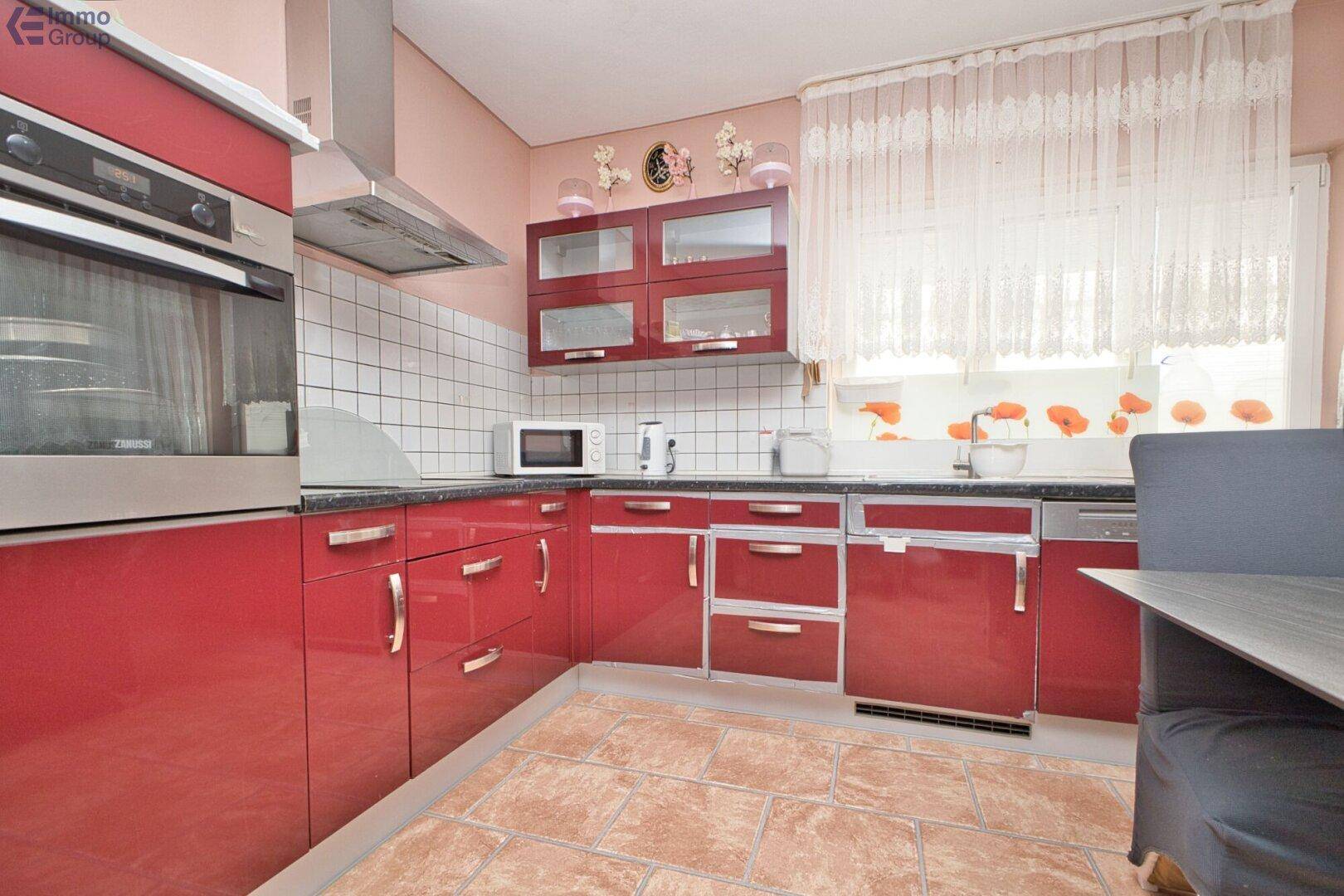 Moderne Küche mit roten Hochglanzfronten, integriertem Backofen und Fliesenboden.