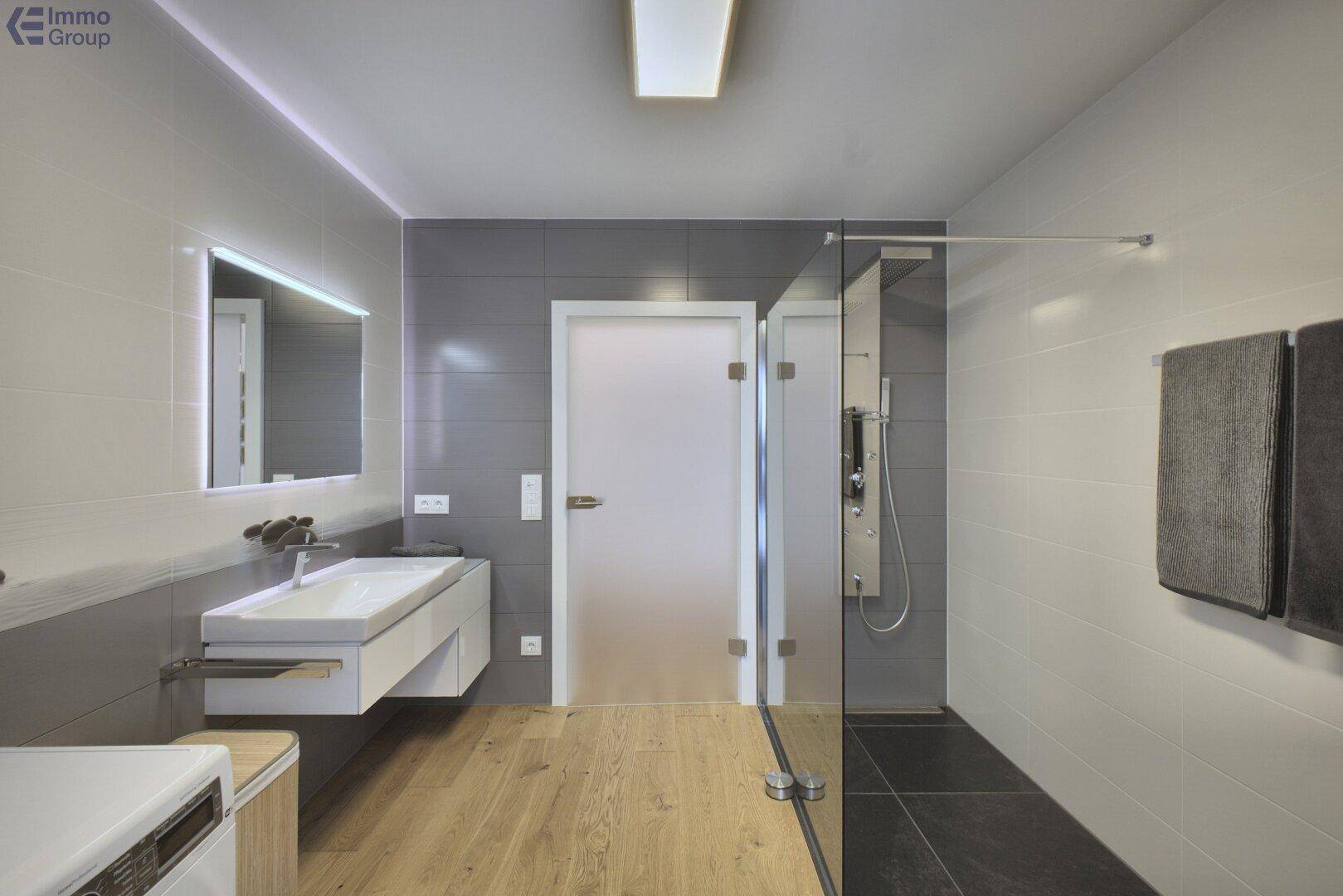 Modernes Badezimmer mit großer Dusche, Waschbecken und Waschmaschine.