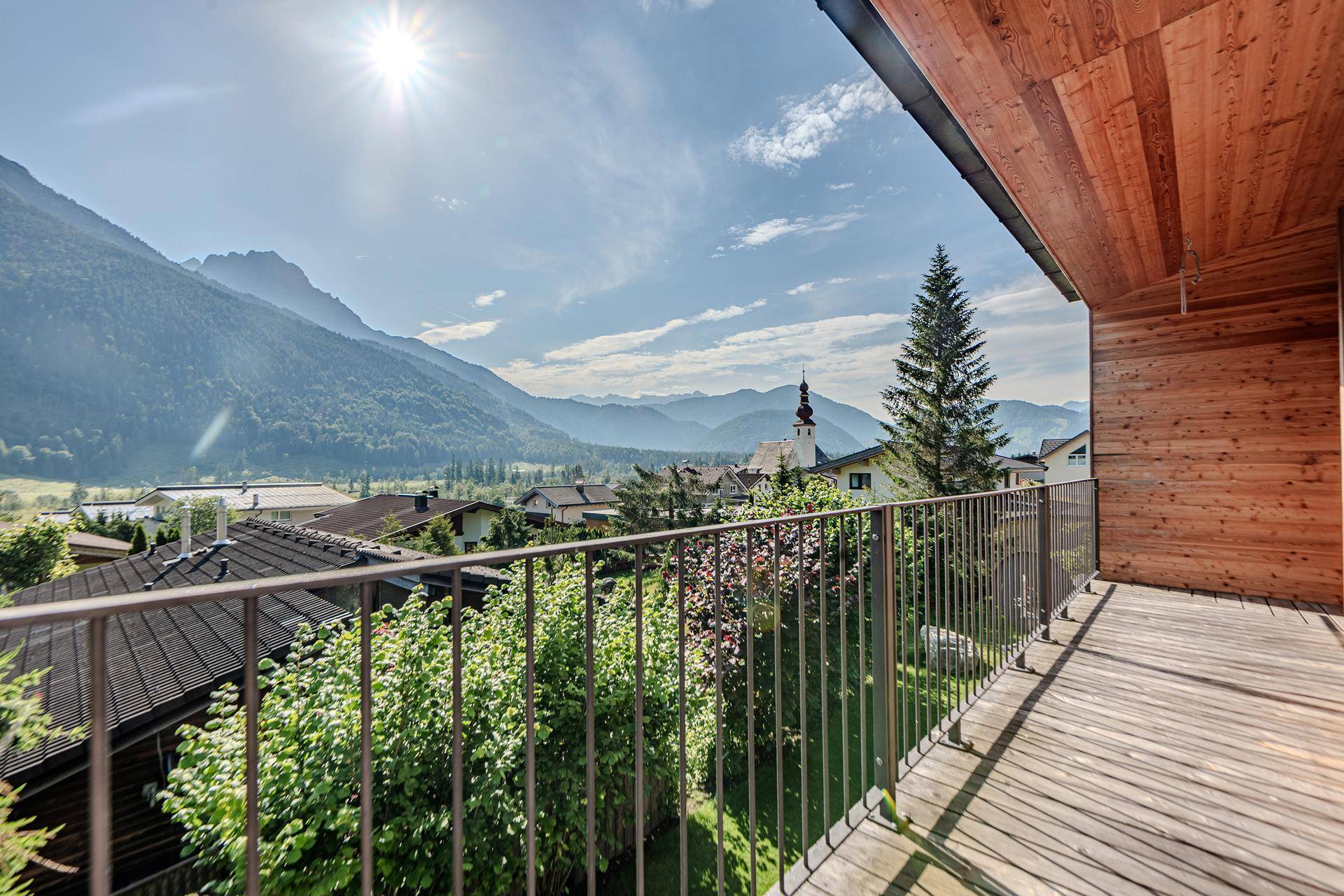 Sonniger Balkon mit Holzboden und weitem Blick über das Tal und die umliegenden Berge.
