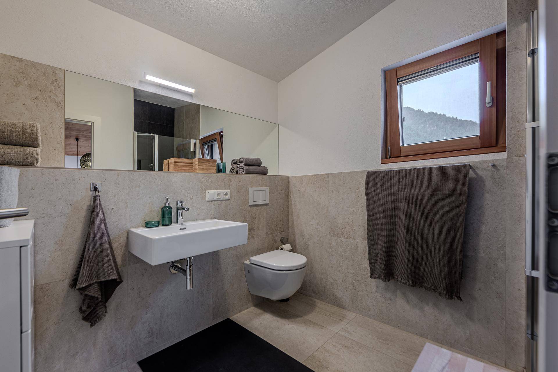 Modernes Gäste-WC mit wandhängender Toilette, Waschbecken und Fenster für natürliche Belüftung.