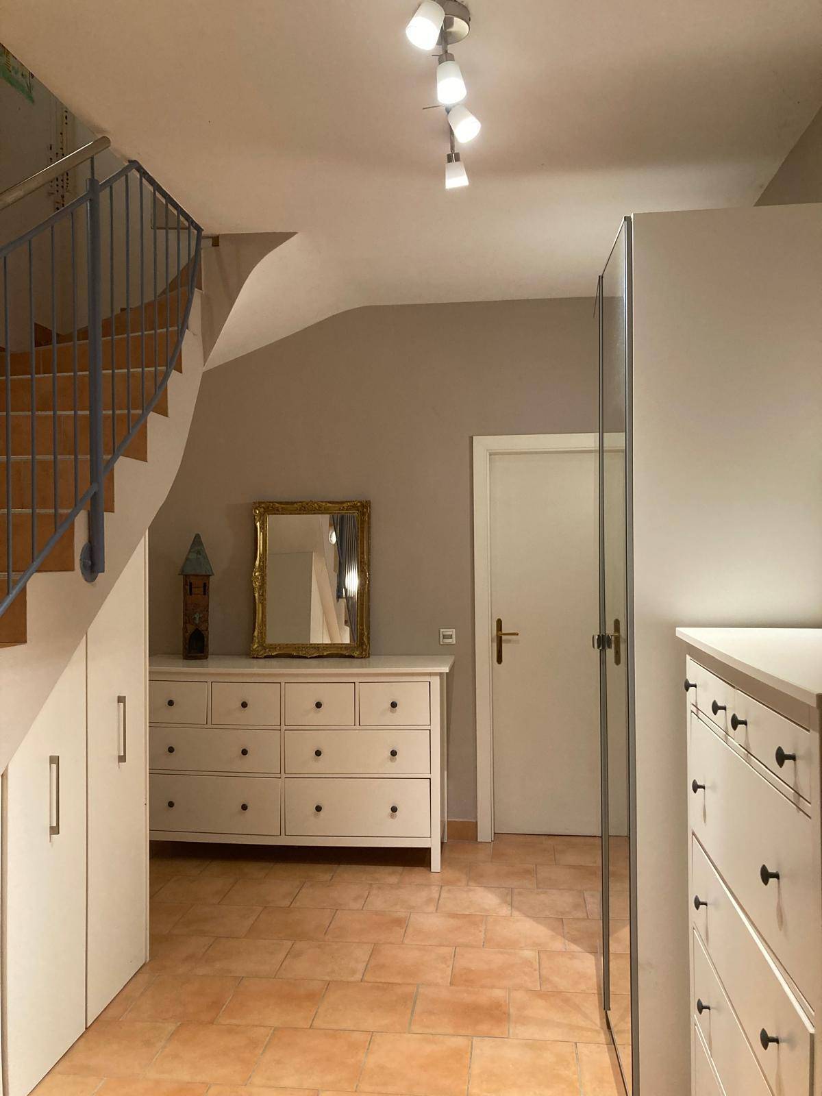 Heller Flur mit Kommode, Spiegel und integrierten Schränken unter der Treppe.