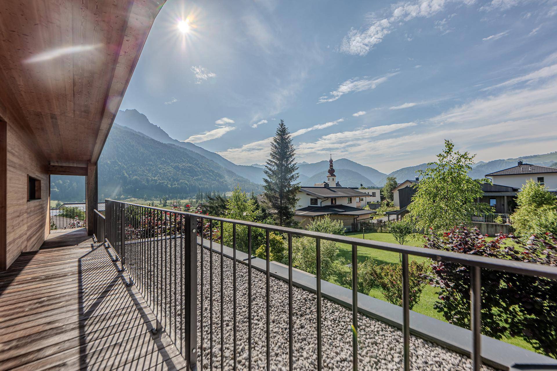 Geräumiger Balkon mit Holzboden und Panoramablick auf die Berglandschaft und das charmante Dorf.