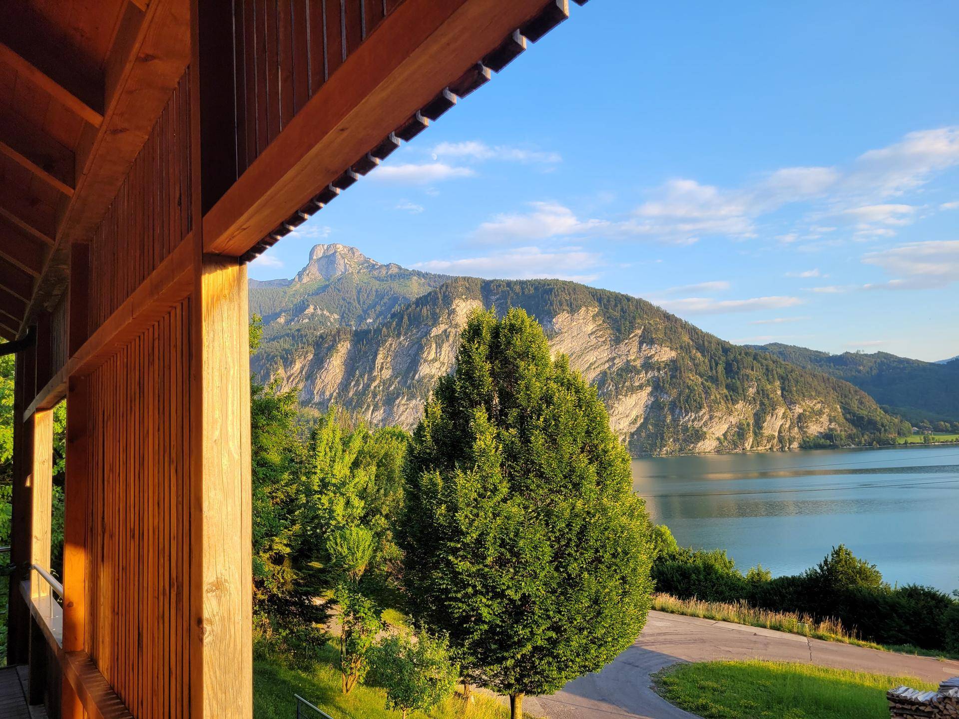 Malerischer Ausblick von der Holzloggia auf den glitzernden See und die majestätischen Berge unter strahlend blauem Himmel.
