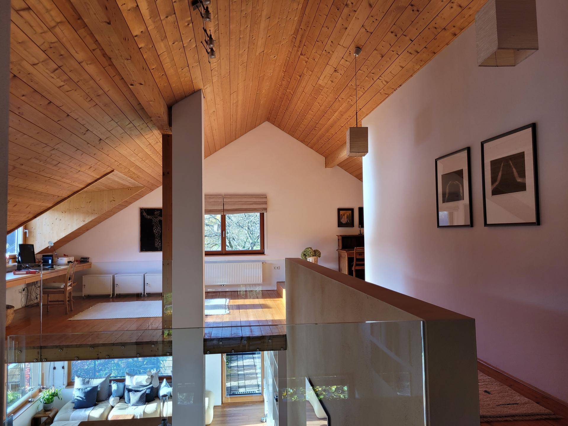 Offene Galerie mit Holzboden und schrägen Decken, die einen Blick auf den darunterliegenden Wohnbereich bietet.