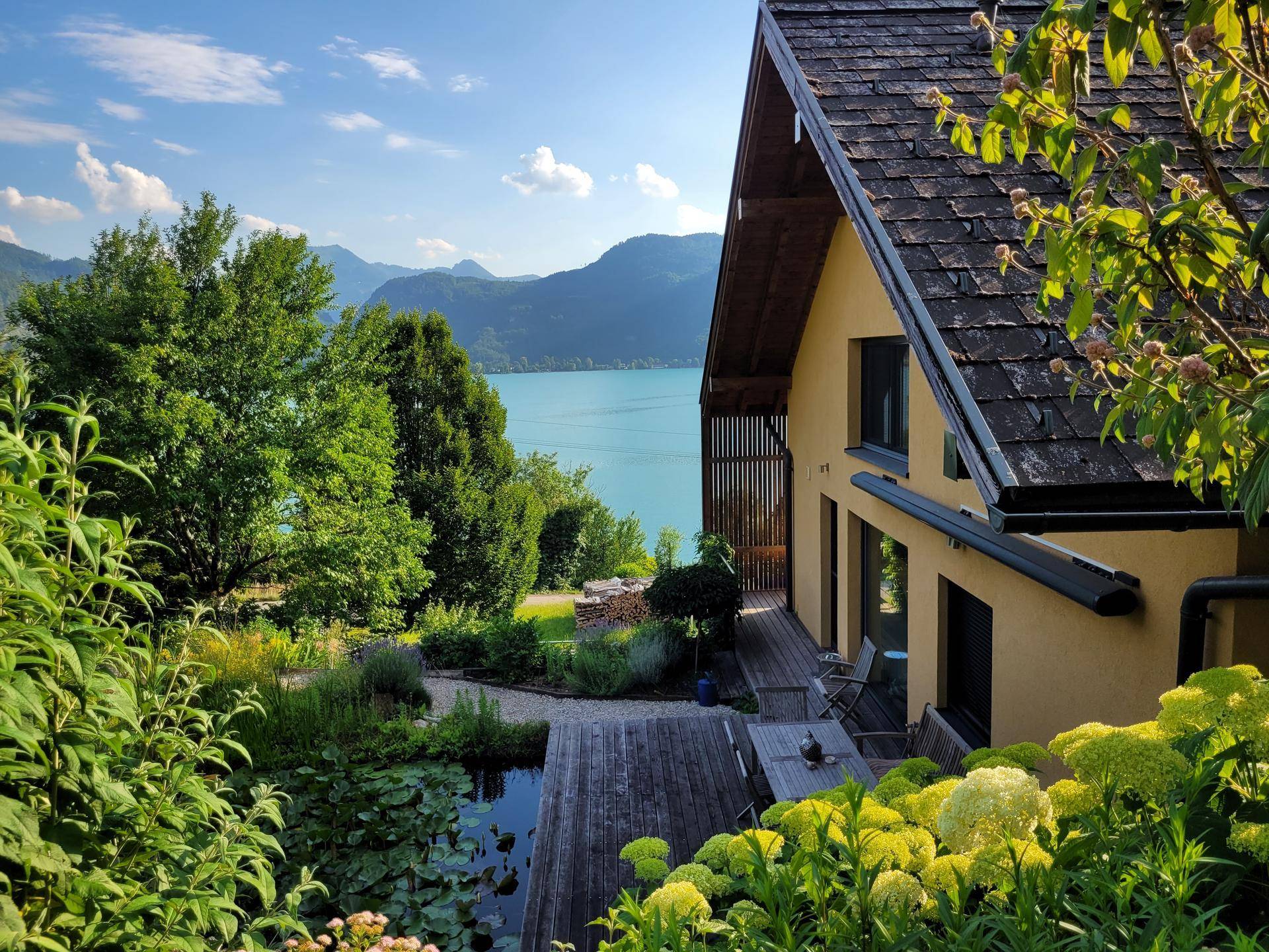 Charmantes Haus mit Holzterrasse und Teich, bietet einen atemberaubenden Blick auf den See und die umliegenden Berge.
