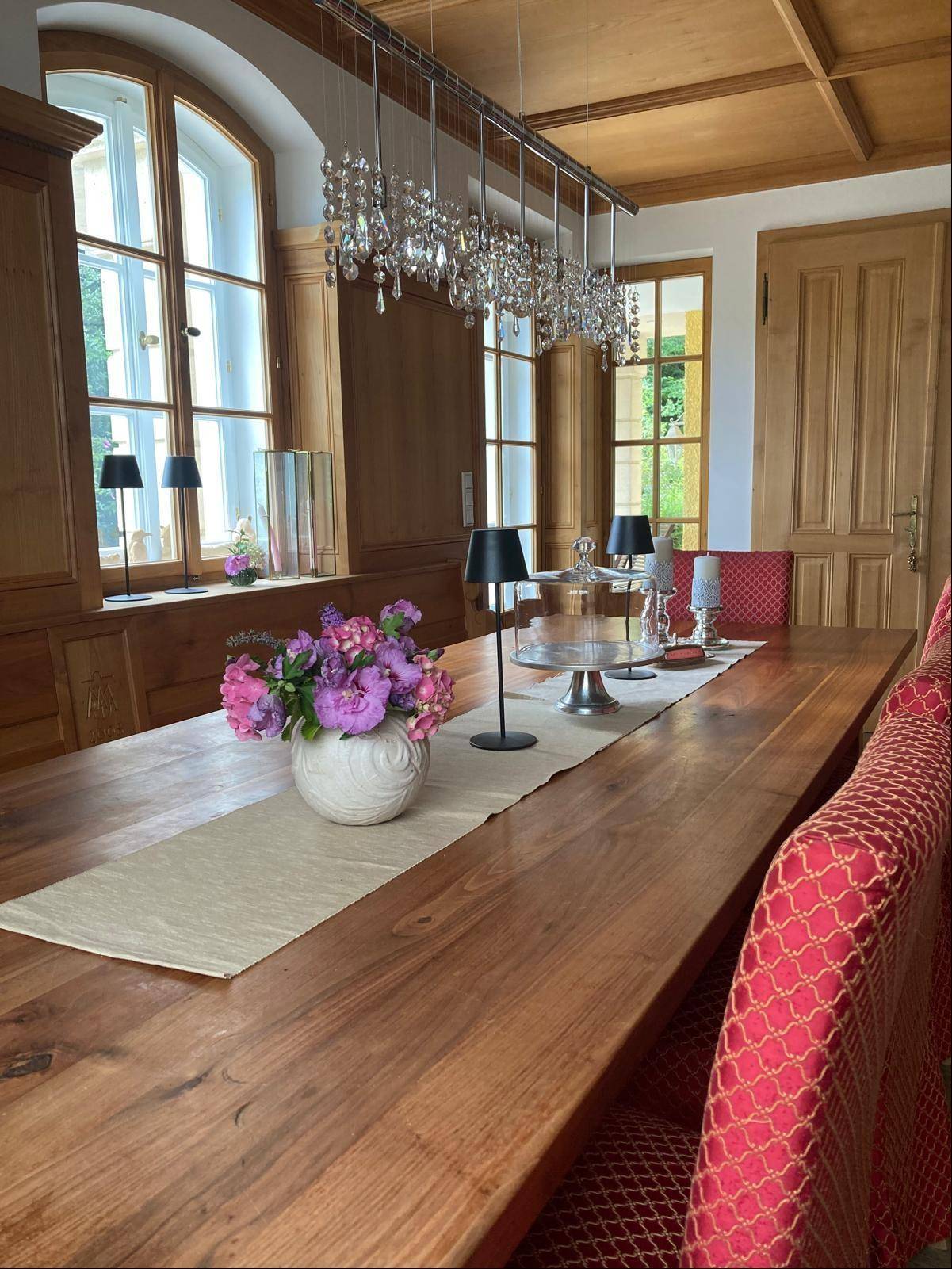 Großzügiges Esszimmer mit langem Holztisch, Kronleuchter und Holztäfelung.