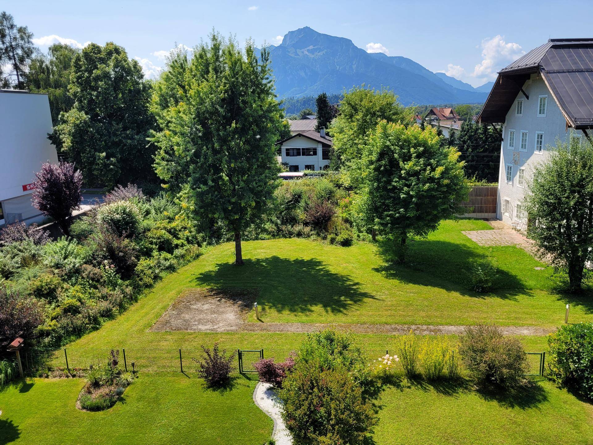 Großer, gepflegter Garten mit Rasenfläche, Bäumen und Bergblick im Hintergrund.