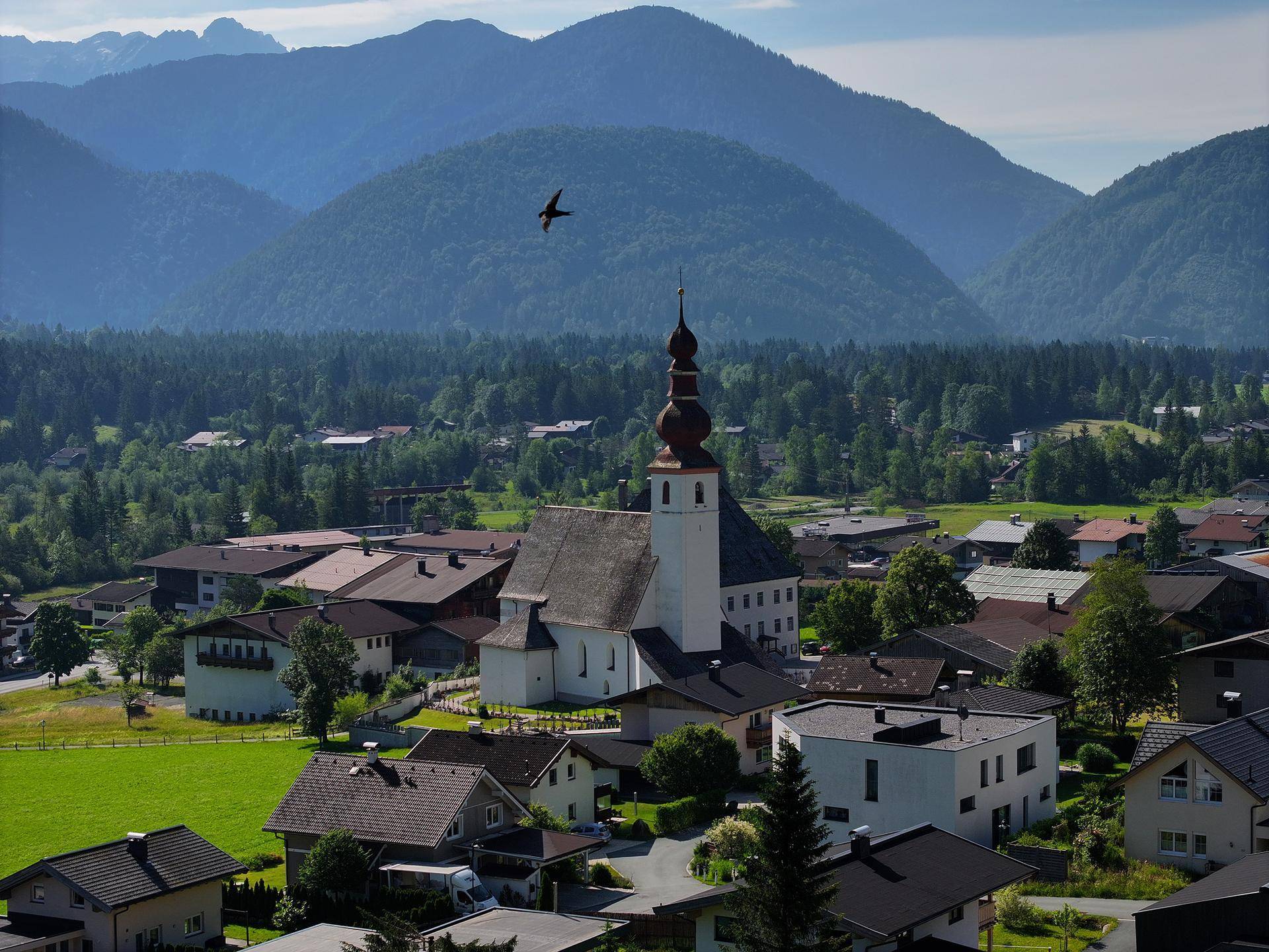 Malerische Ansicht des Dorfes mit Kirche, umgeben von grünen Wäldern und majestätischen Bergen.