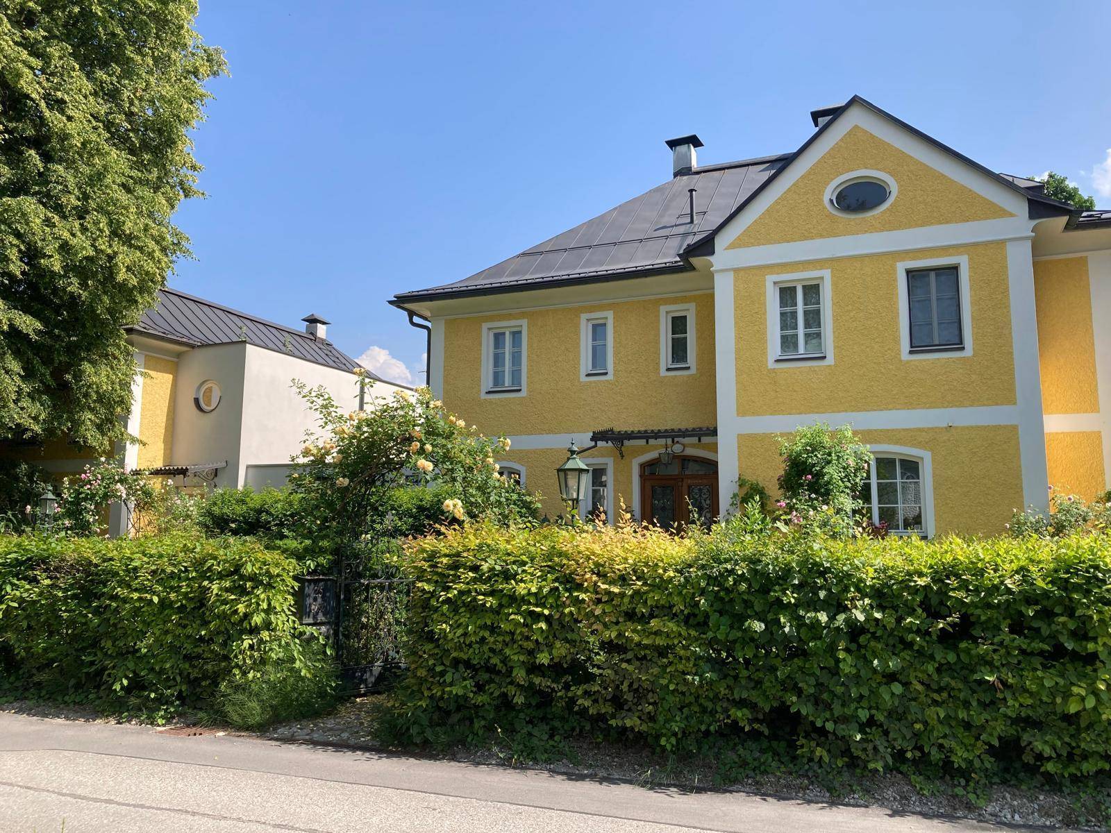 Charmante Villa mit gelber Fassade und gepflegter Hecke an der Straßenseite.