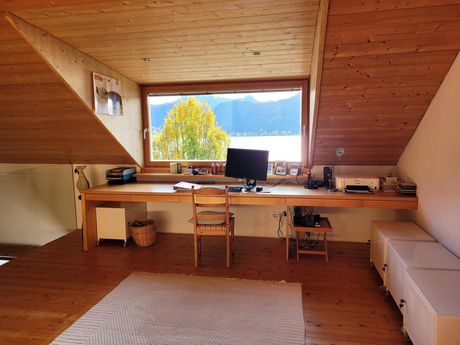 Helles Büro im Dachgeschoss mit großem Schreibtisch und weitem Blick auf den See und die Berge.