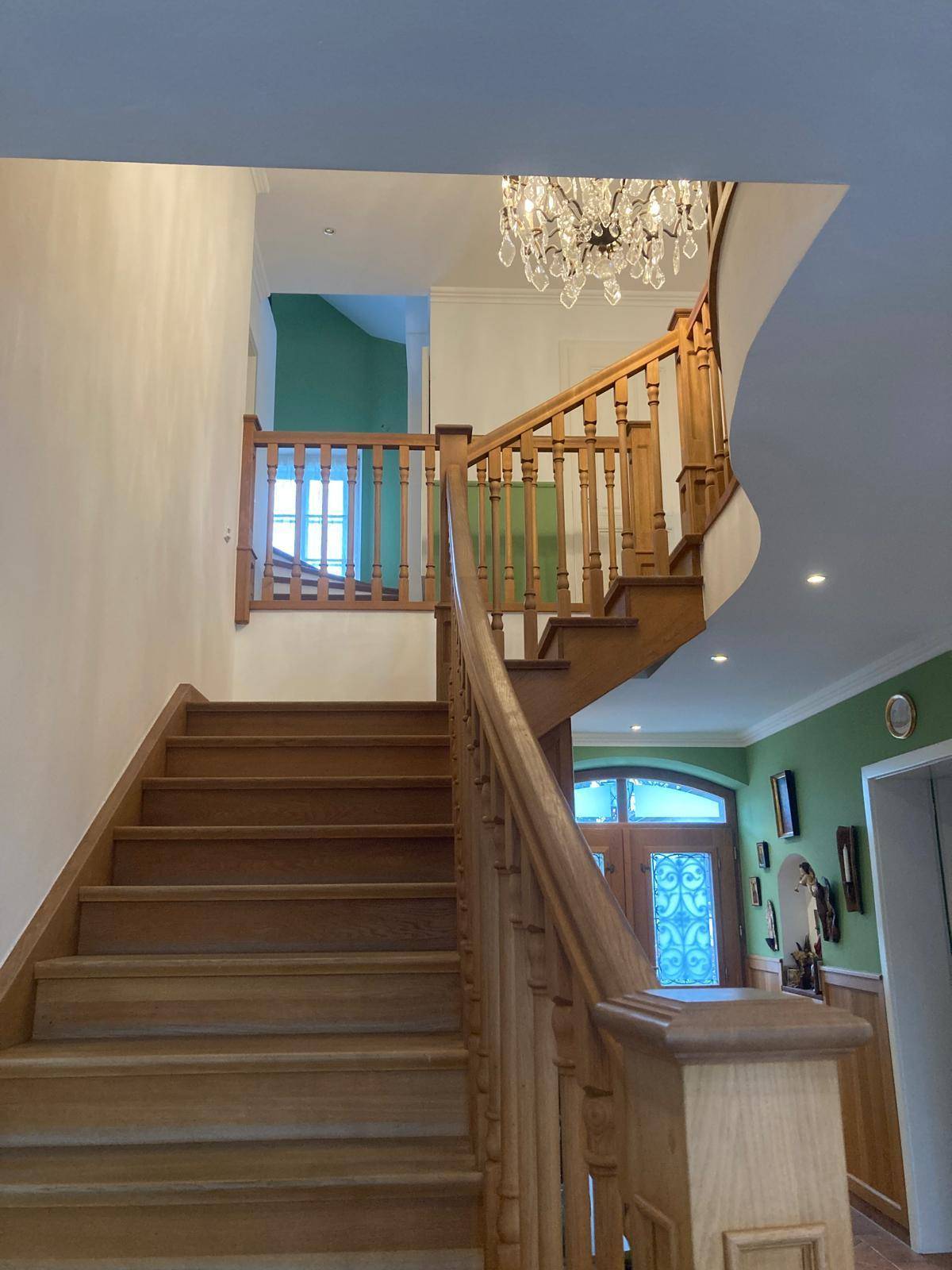 Elegante Holztreppe mit geschwungenem Geländer und Kronleuchter im Treppenhaus.