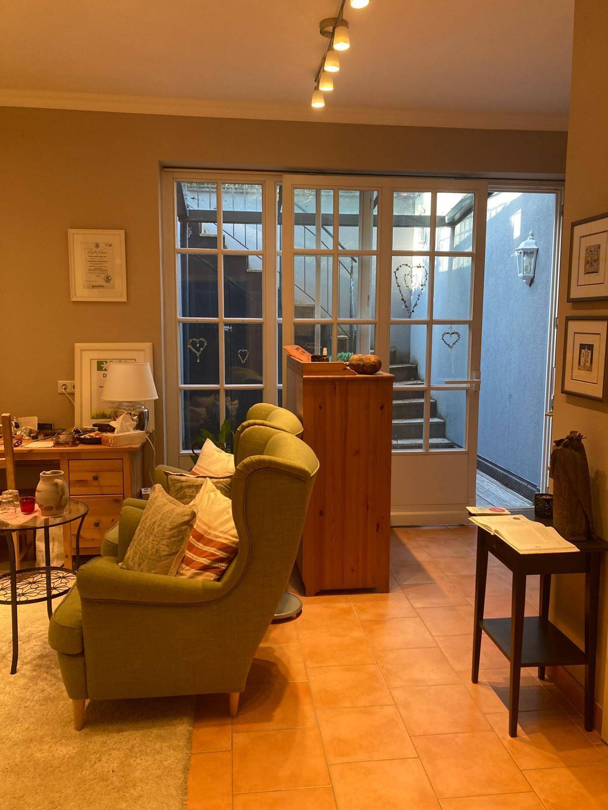 Gemütliches Wohnzimmer mit grünen Sesseln und Blick auf einen überdachten Außenbereich.
