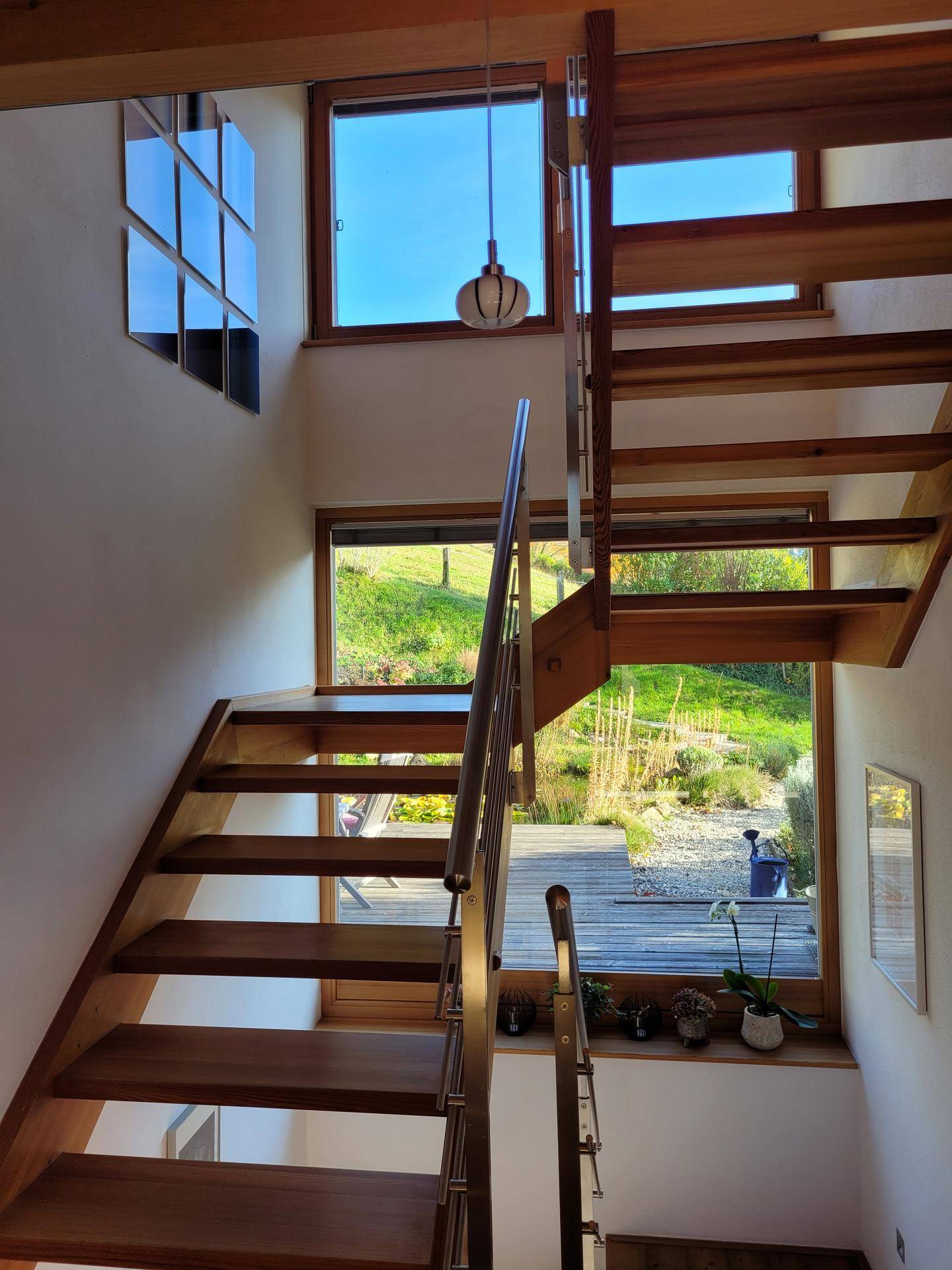 Helle Holztreppe mit Edelstahlgeländer und großen Fenstern, die einen Blick in den Garten ermöglichen.