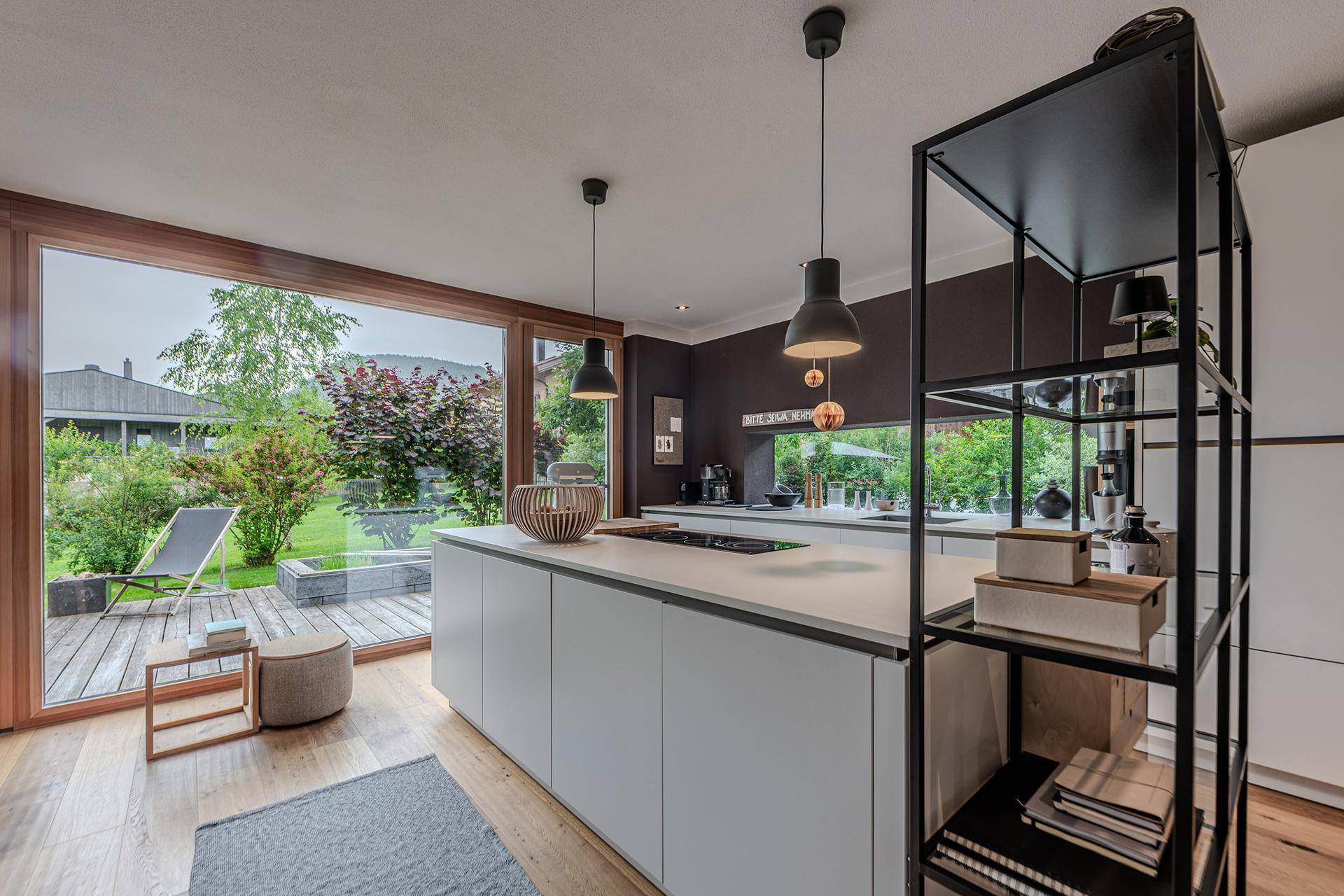 Moderne Küche mit weißer Kochinsel, Holzboden und großen Fenstern zur Terrasse und zum Garten.